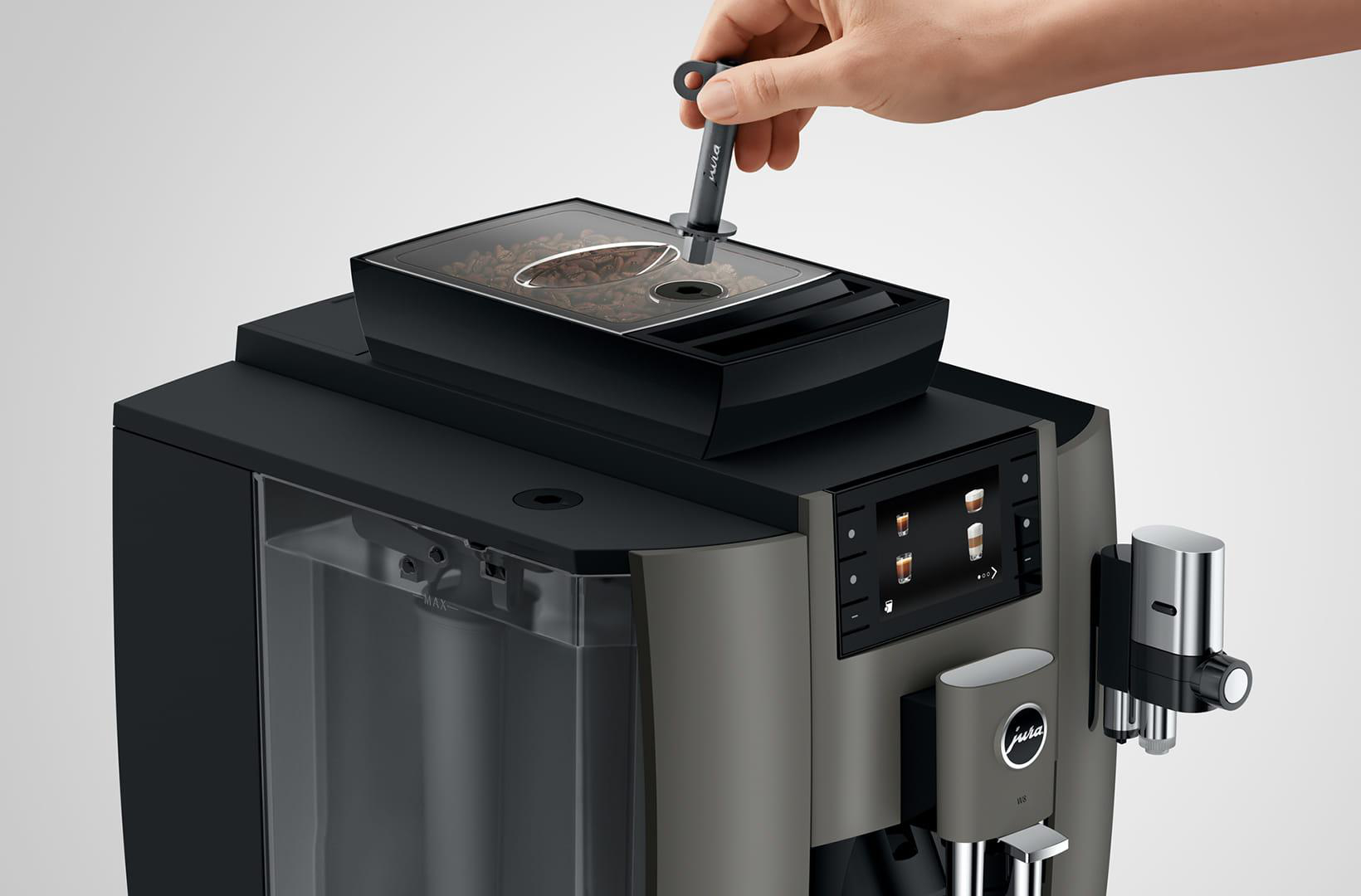 Eine Person, die Kaffeebohnen in die Oberseite einer schwarz-grauen Kaffeemaschine gibt.