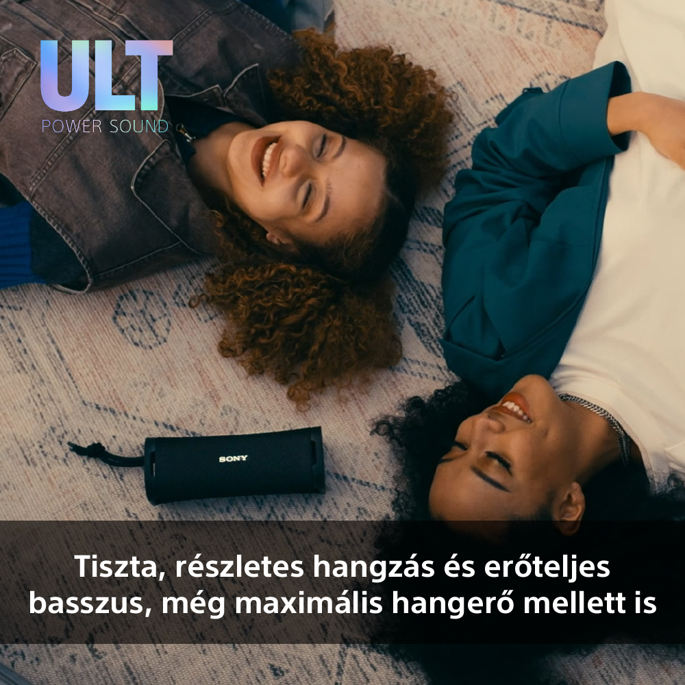Két mosolygó nő szőnyegen fekszik. Egy fekete hangszóró van a szőnyegen mellettük.