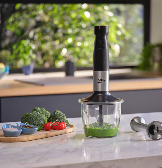 Blender ręczny Beko w użyciu. Szklany pojemnik z zmiksowanym zielonym jedzeniem. Brokuły i pomidory po lewej.