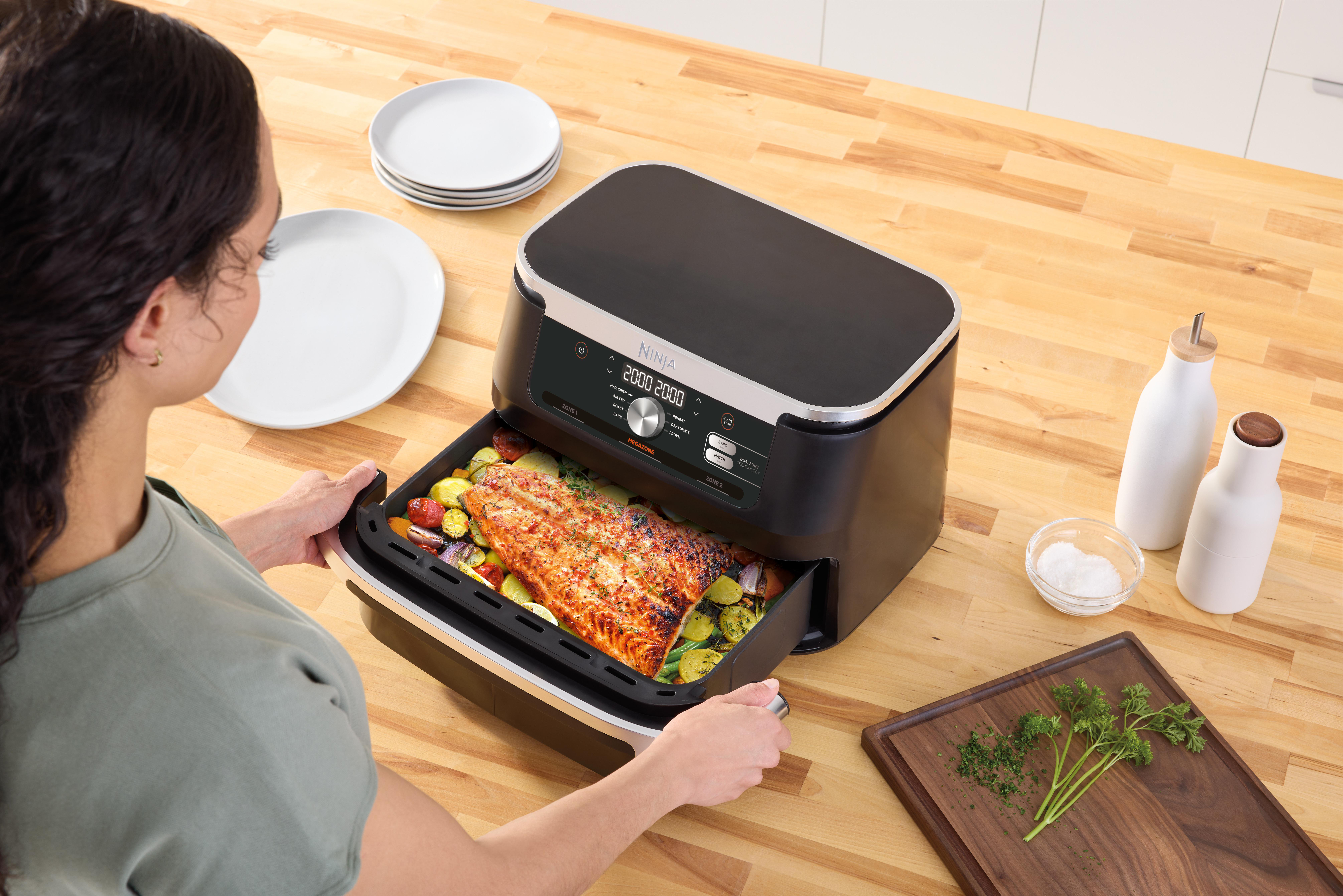 Frau mit Heißluftfritteuse mit Lachs und Gemüse auf einem Tisch.