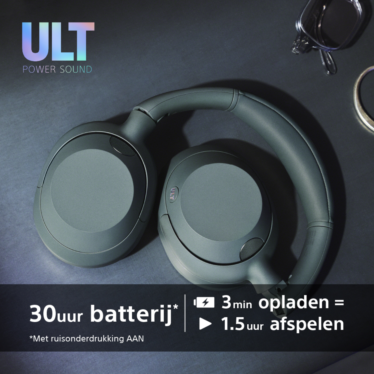 Dark green headphones with text about battery life. The background is dark with some other items.