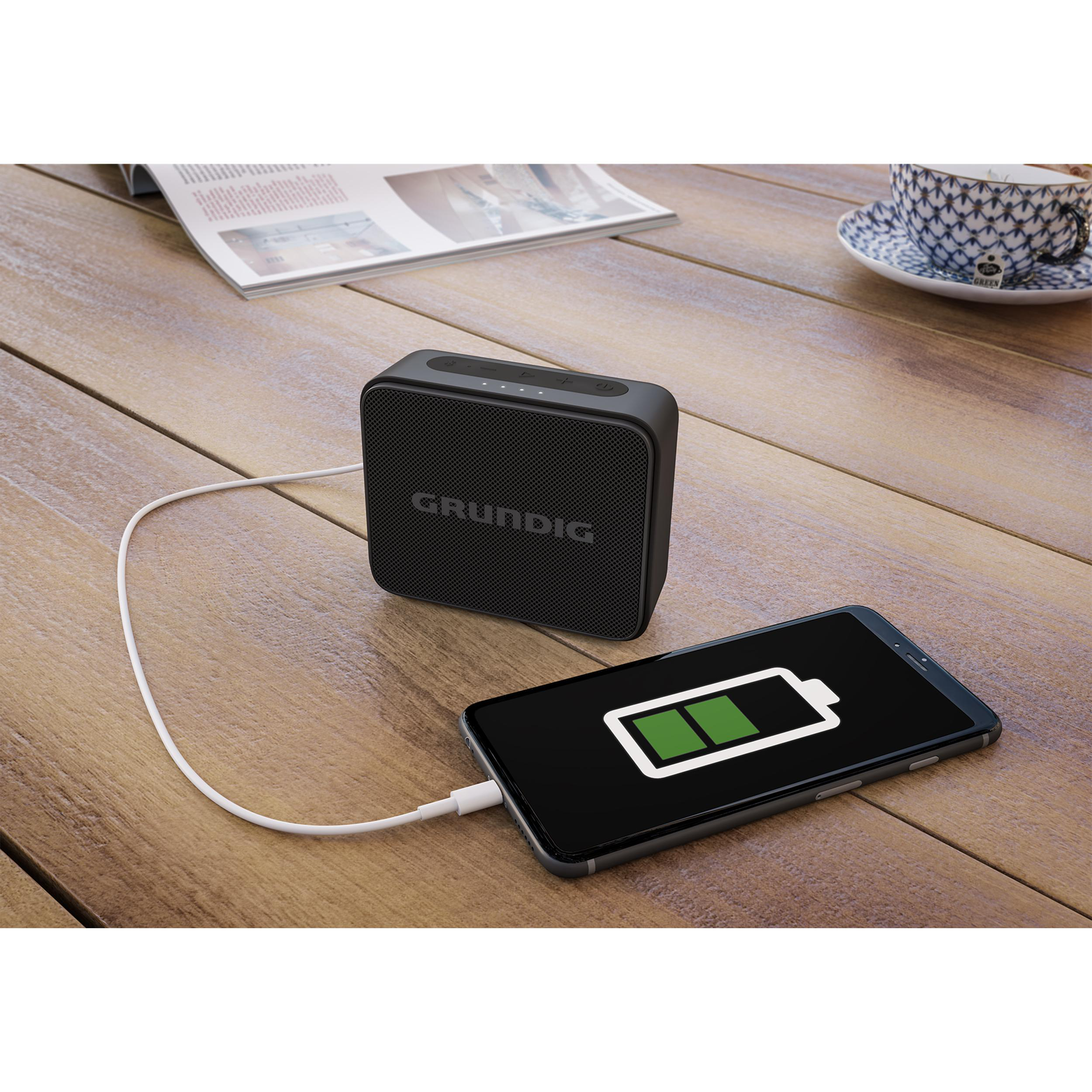 Schwarzer Grundig-Lautsprecher und Telefon laden auf einem Holztisch, mit Kaffeetasse.