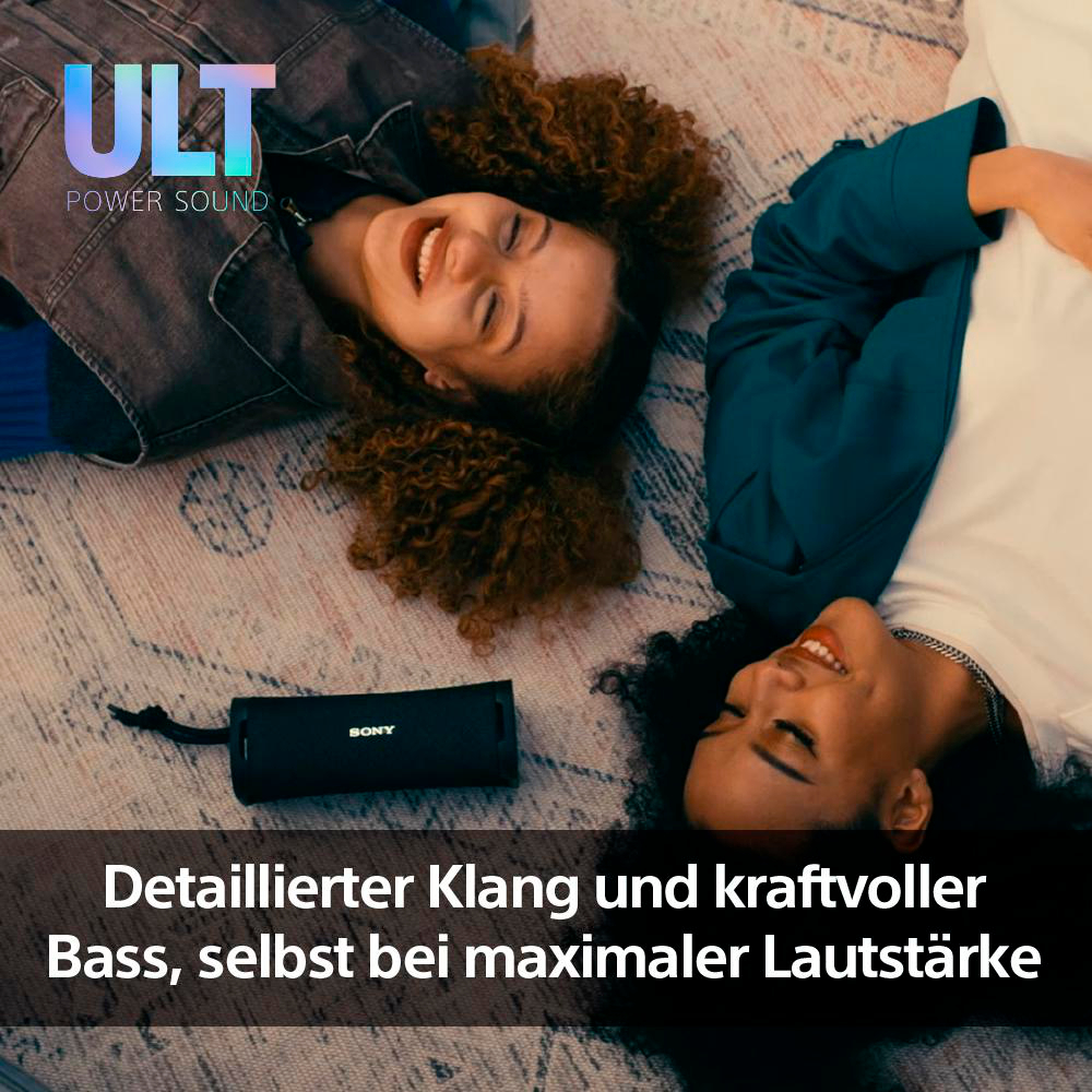 Zwei Frauen lachen, auf einem gemusterten Teppich liegend. Zwischen ihnen liegt ein schwarzer Lautsprecher. Text unten.