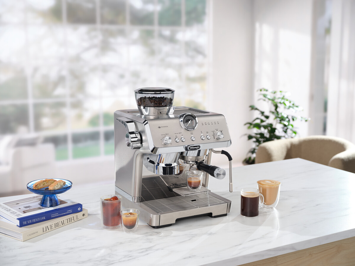 Eine Espressomaschine aus Edelstahl auf einer Marmoroberfläche mit Kaffeetassen und einem Dessert.