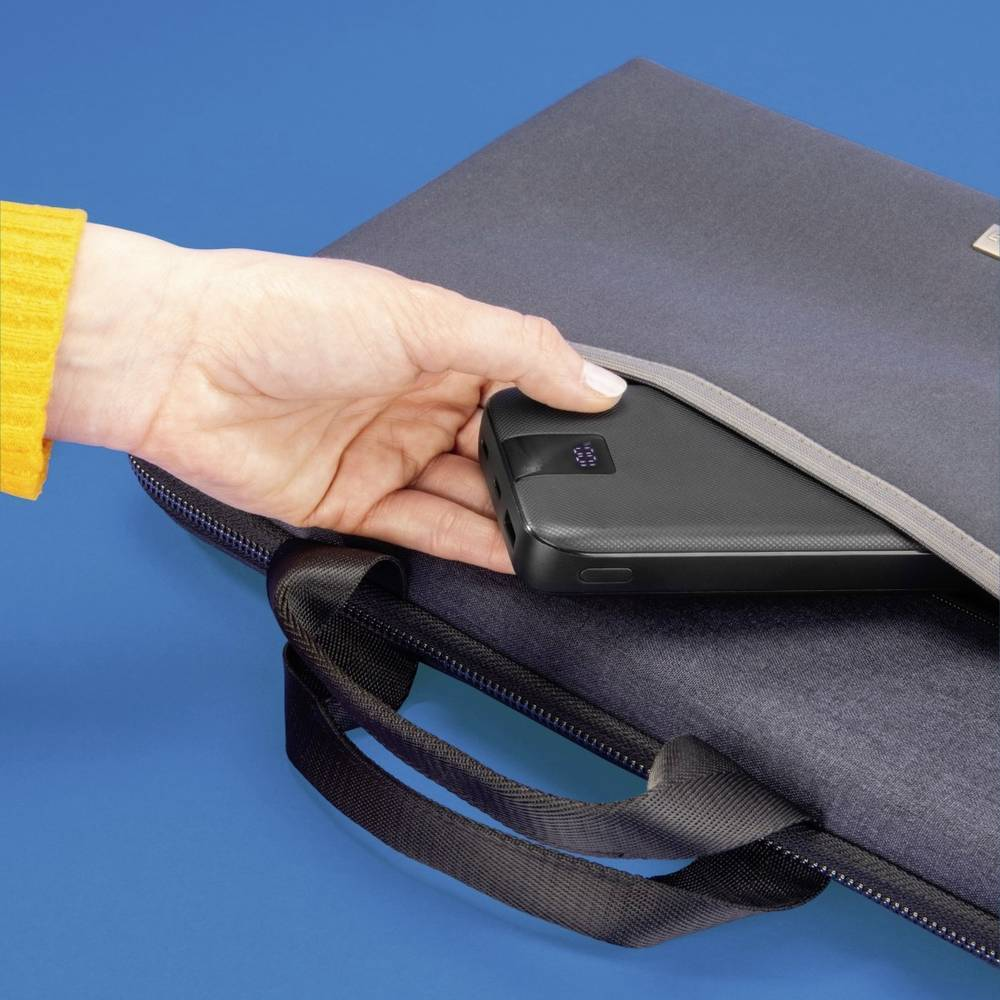 Ręka wkładająca czarny power bank do szarego etui na laptopa na niebieskiej powierzchni.