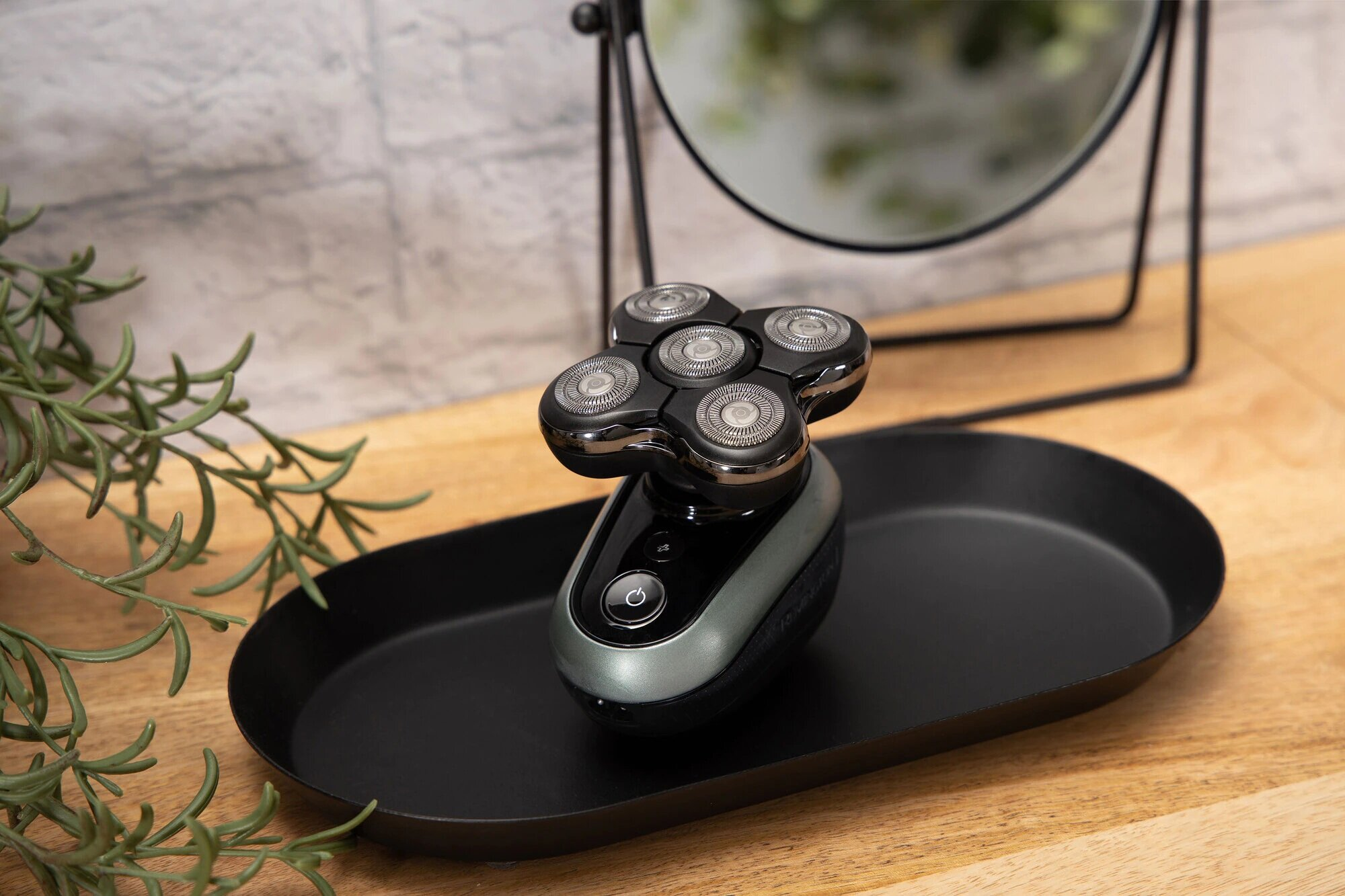 Golarka elektryczna na czarnej tacy na drewnianym stole, lustro, kwiatowe tło.