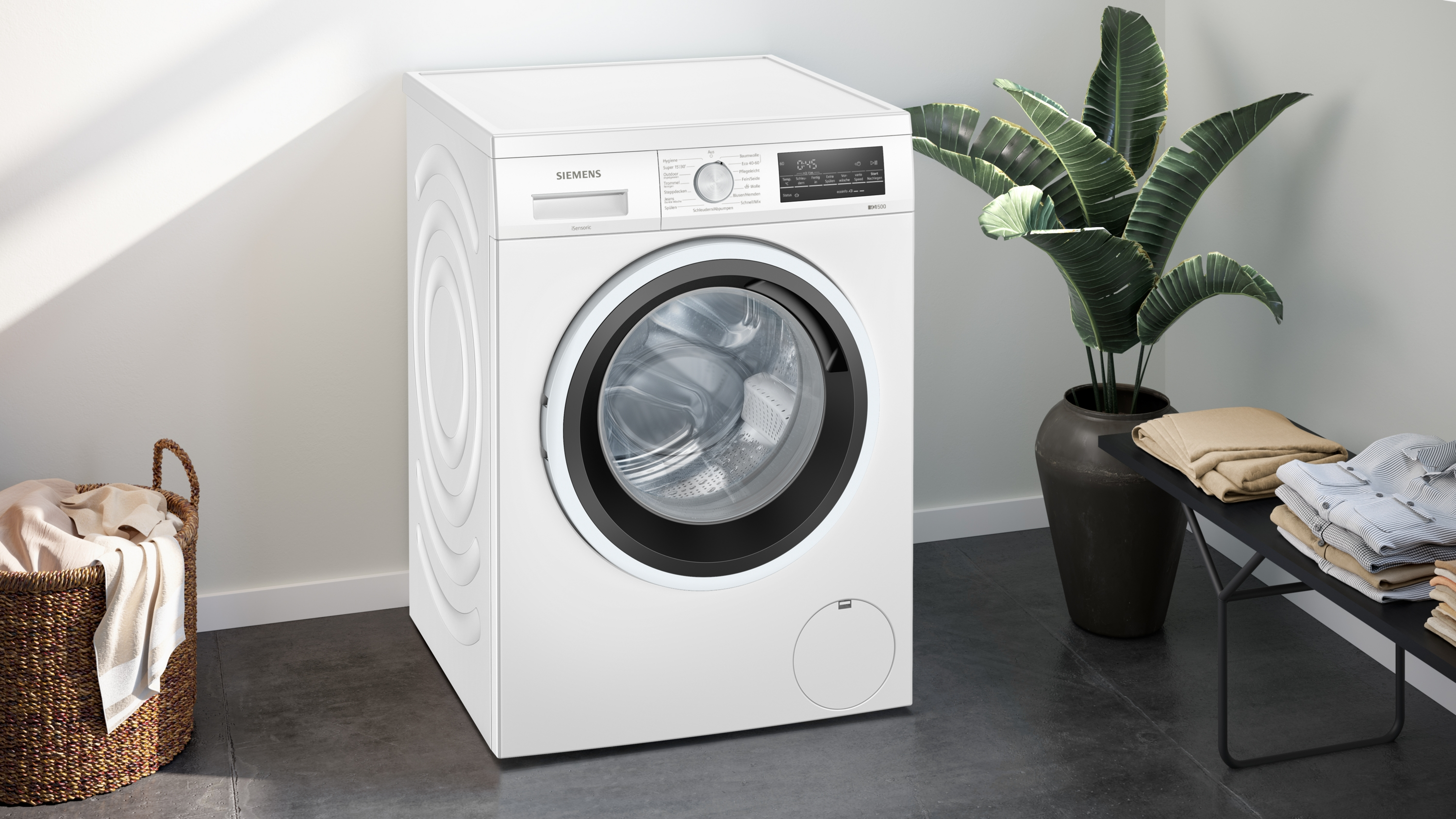 Weiße Siemens Waschmaschine neben einem Korb und einer Pflanze.