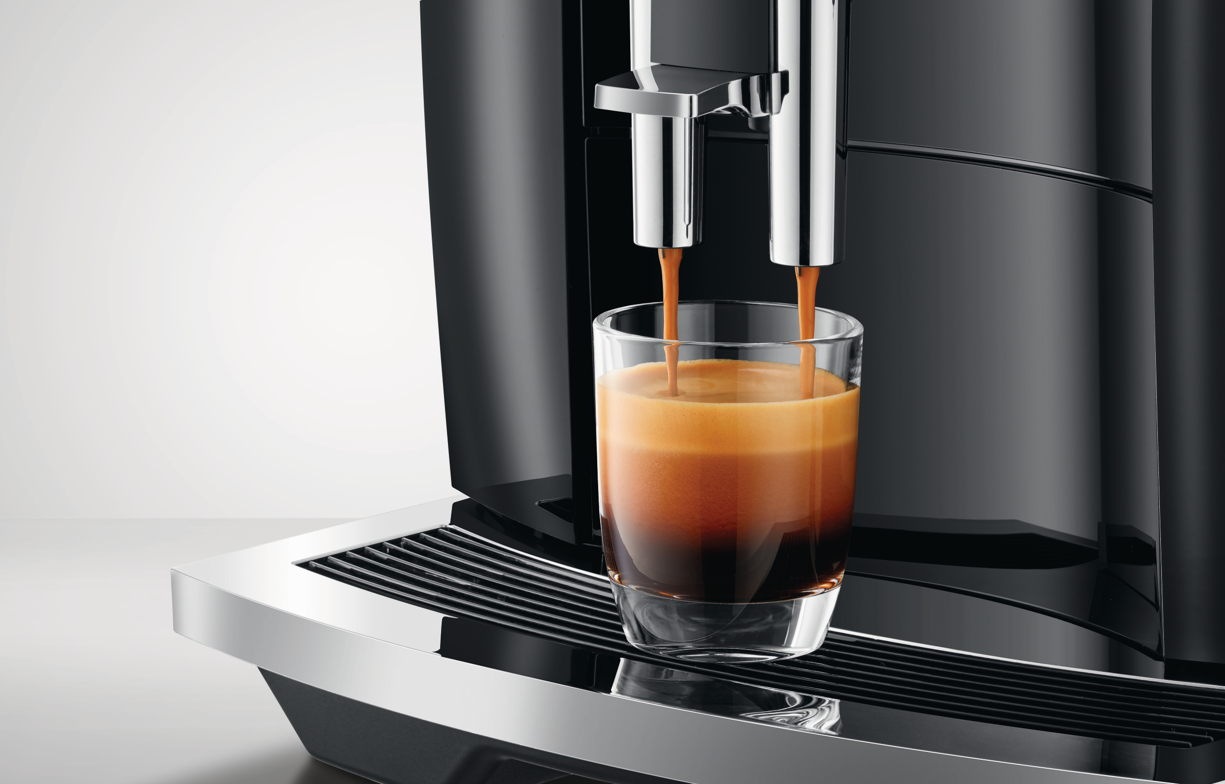 Eine Kaffeemaschine, die Kaffee in ein Glas gießt. Schwarze Maschine, weißer Hintergrund.
