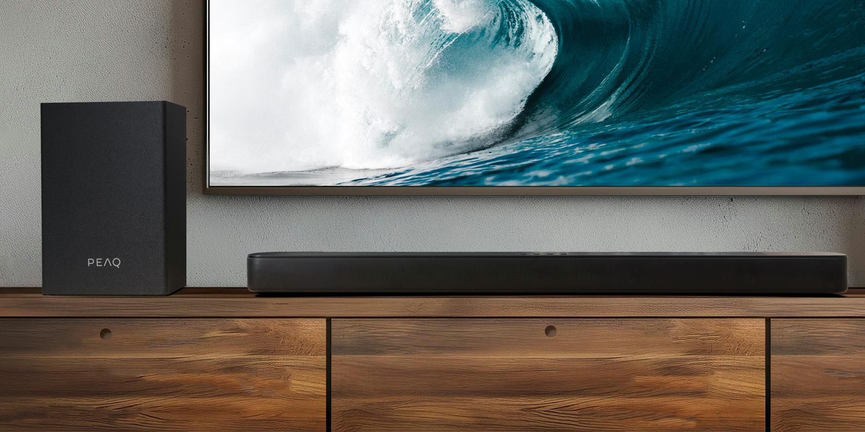 Schwarze Soundbar und Subwoofer auf Holzschrank. Eine große Welle wird auf dem Fernsehbildschirm angezeigt.