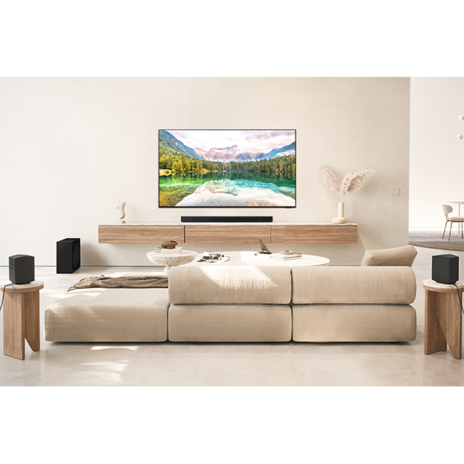 Living room with a large TV, soundbar, two speakers, and a beige couch. The room is well lit.