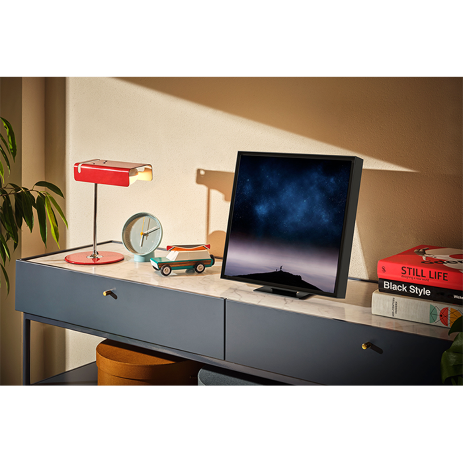 A TV on a desk with decorations: a lamp, a clock, a toy car, and books.