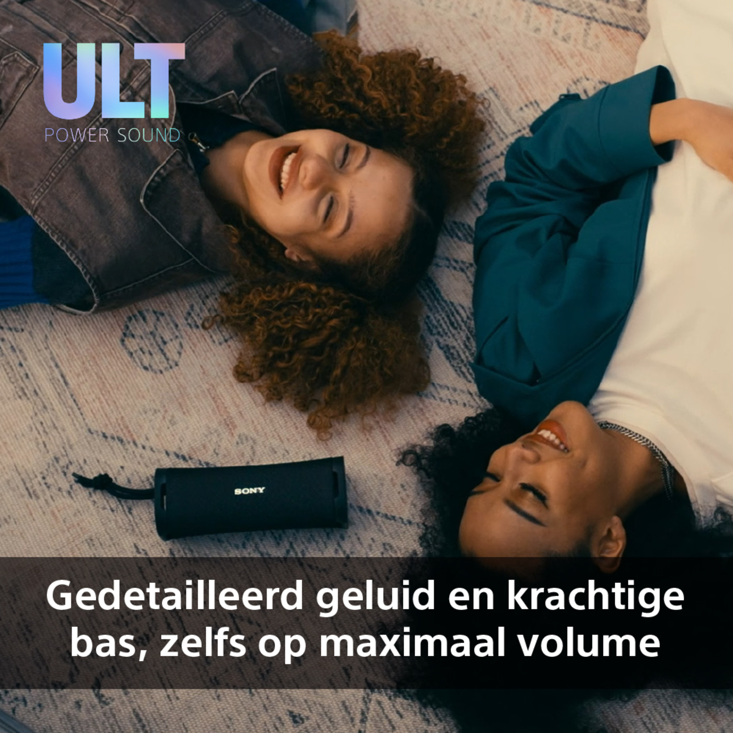 Two women smiling, with a black speaker, and text in Dutch.