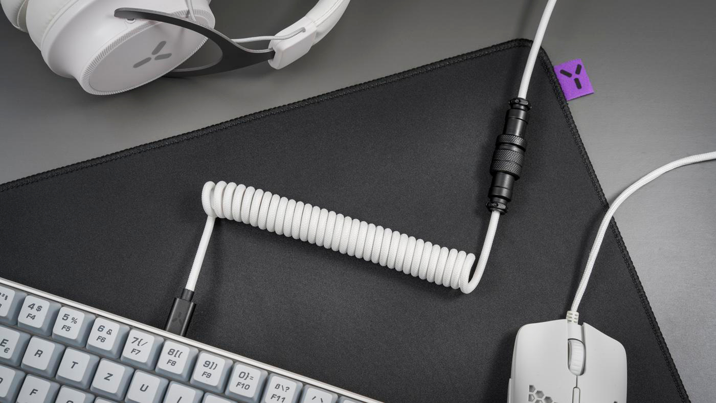 Schreibtisch-Setup mit weißer Tastatur, Maus, Mauspad, Kopfhörern und einem Spiralkabel.