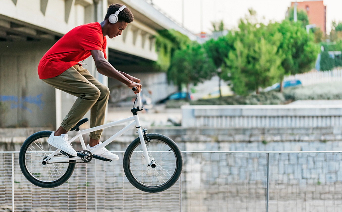 Egy fiatal piros pólóban egy fehér BMX-szel ugrik át egy korláton.