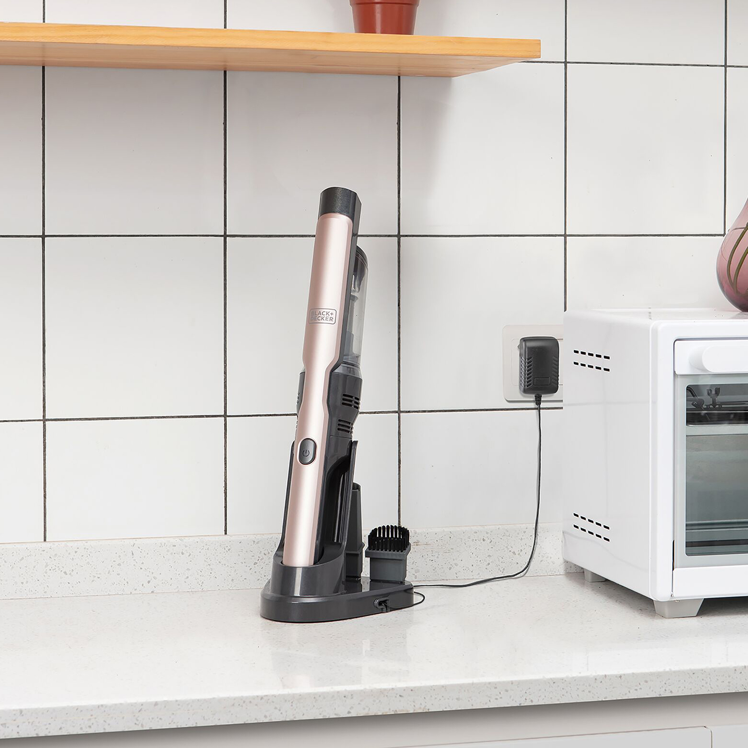 Un aspirapolvere rosa e nero su una base di ricarica, accanto a un forno tostapane bianco.