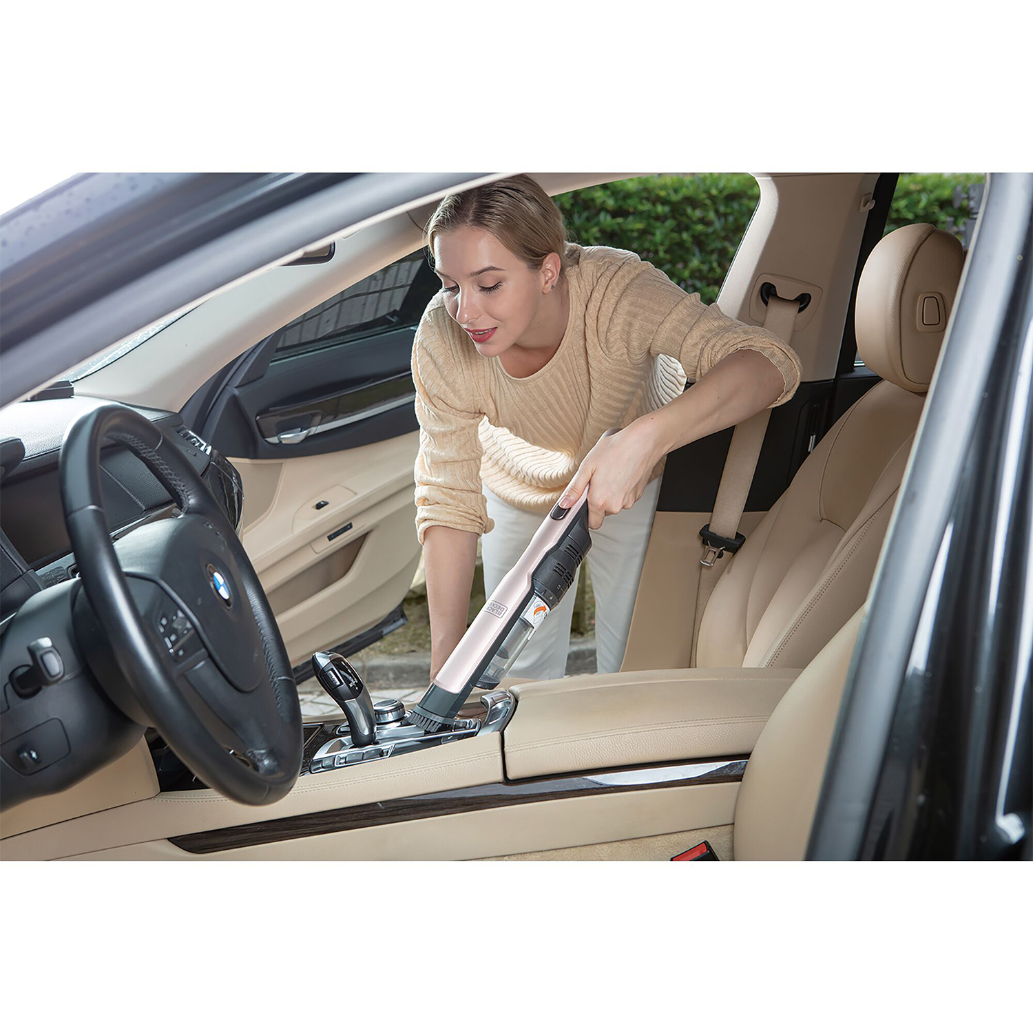 Donna che aspira l'interno dell'auto. L'aspirapolvere è rosa e bianco.