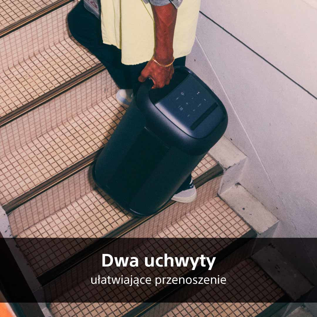 Osoba niosąca czarny głośnik po schodach.