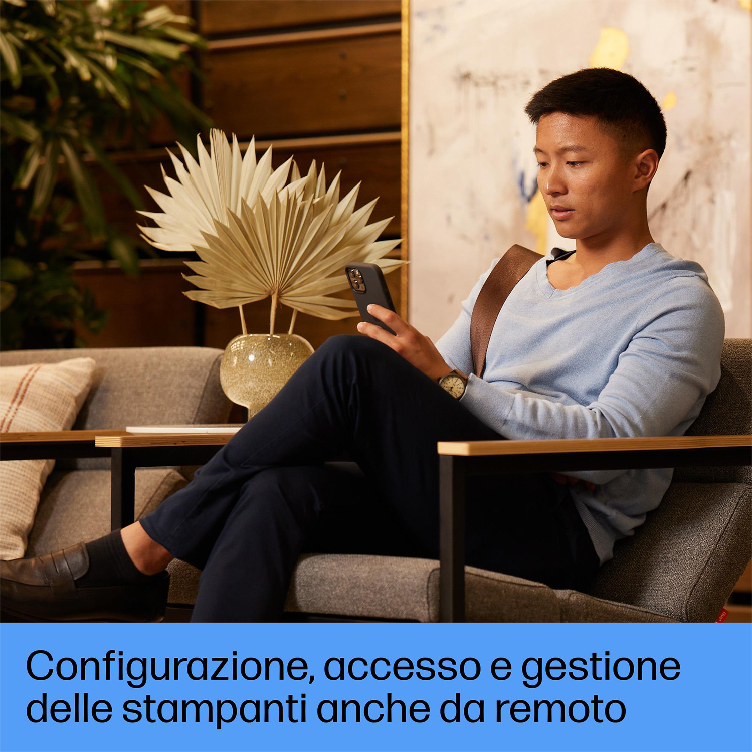 Uomo seduto su un divano, guarda un telefono. Testo in italiano.