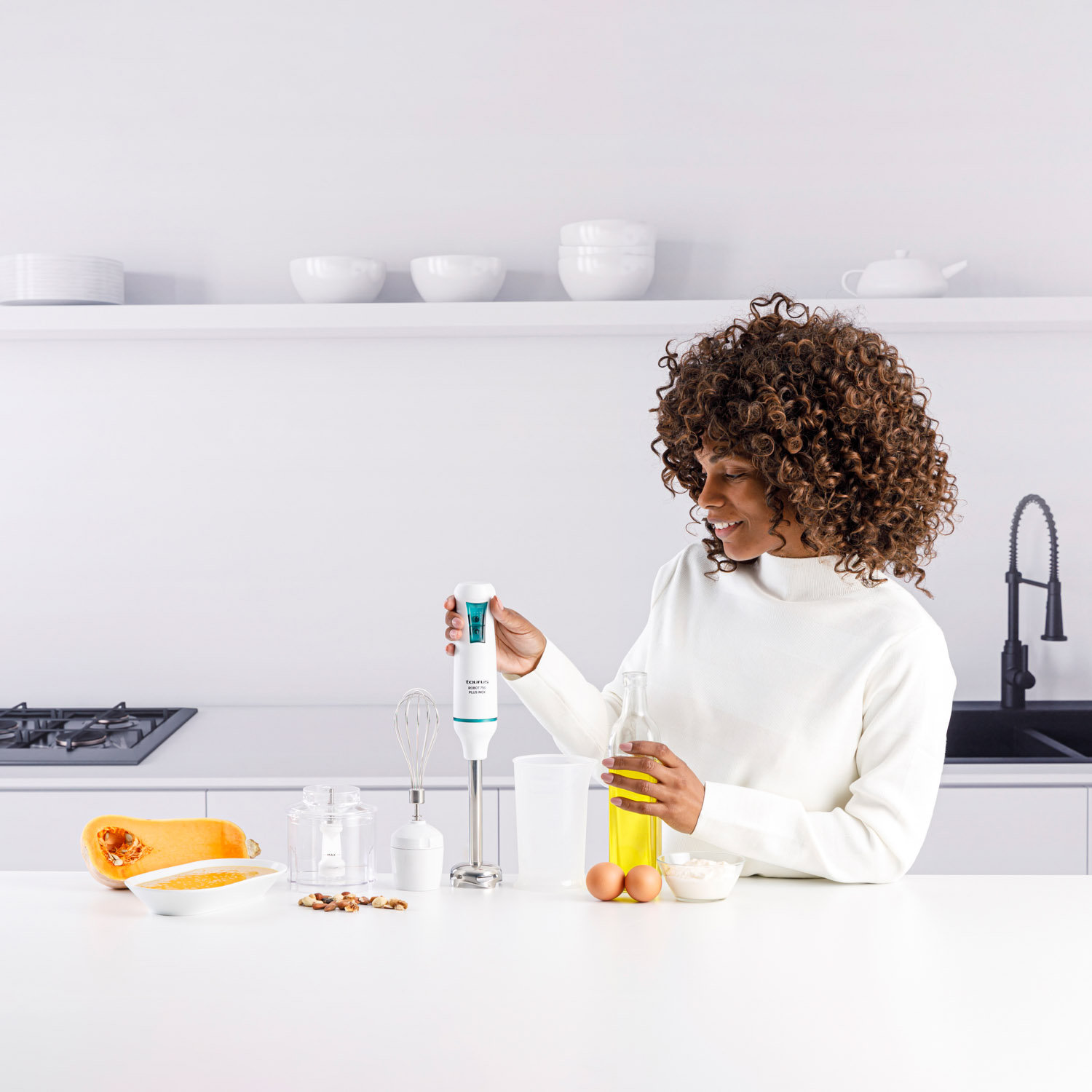 Una mujer preparando comida con una batidora de mano. Hay ingredientes en la encimera.