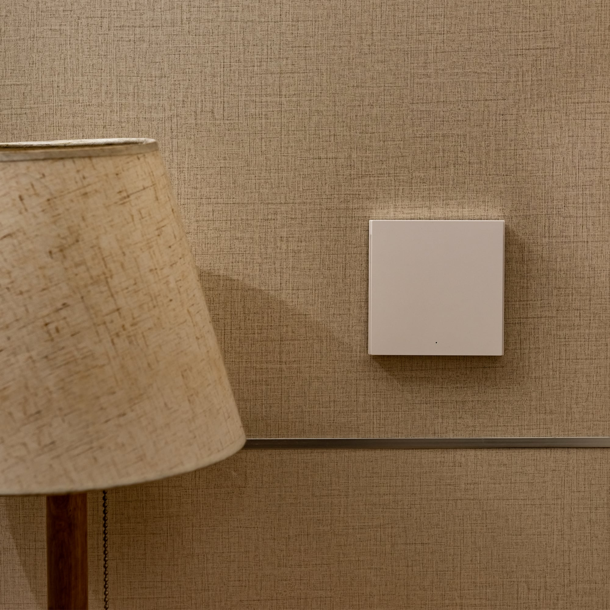 Beige tapeziert. Ein weißer intelligenter Schalter an der Wand. Tischlampe mit beigem Lampenschirm.