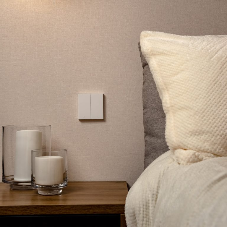 Ein Nachttisch mit Kerzen und einem weißen Lichtschalter an der Wand neben einem Bett.