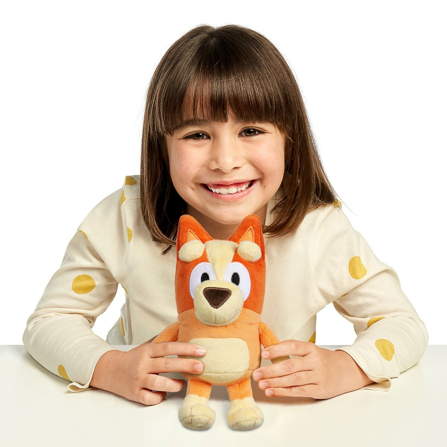 A girl holds a plush toy of a dog. The toy is orange and white.