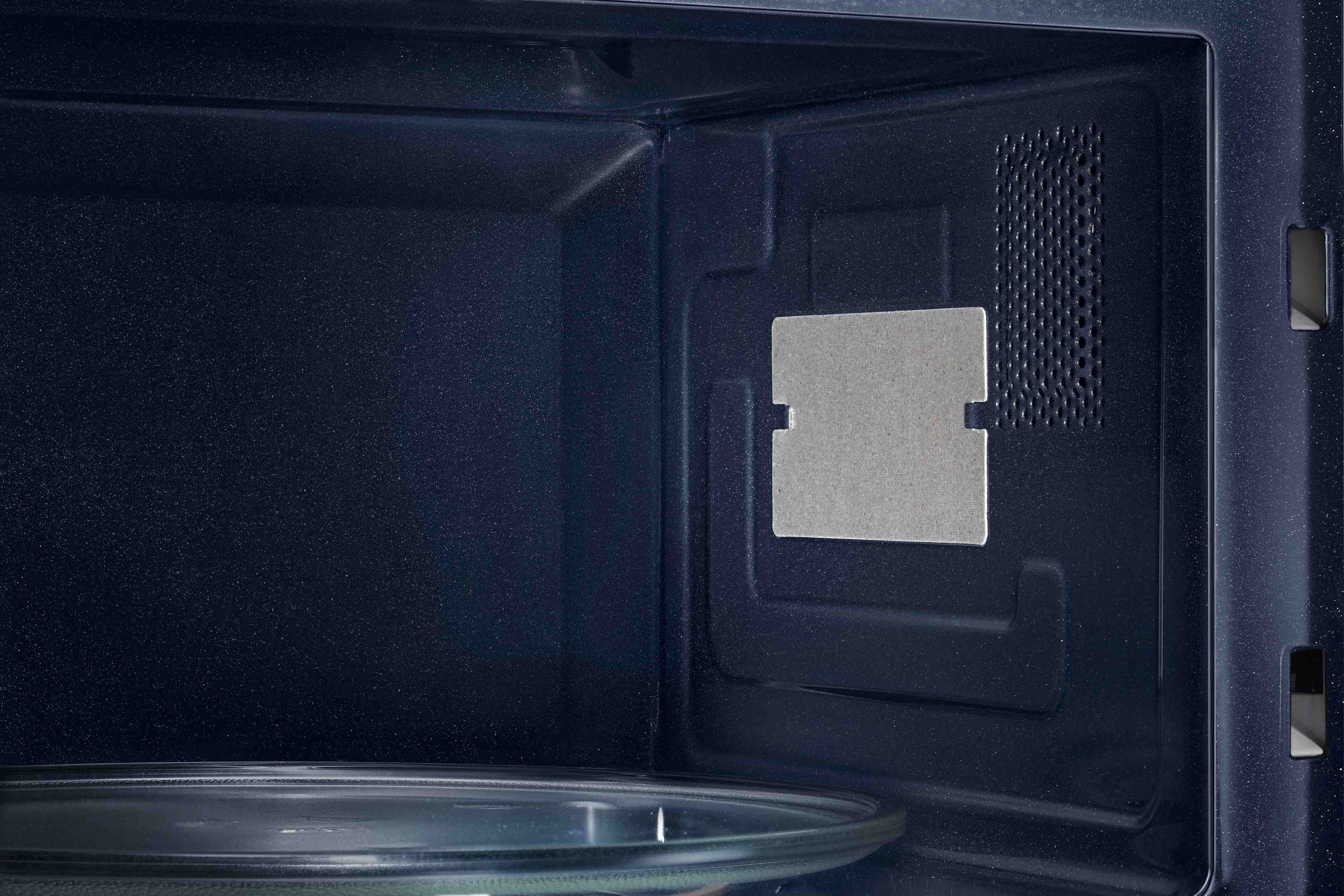 Interno di un forno a microonde blu scuro. C'è una piastra di vetro in basso e una parte rettangolare sul lato.
