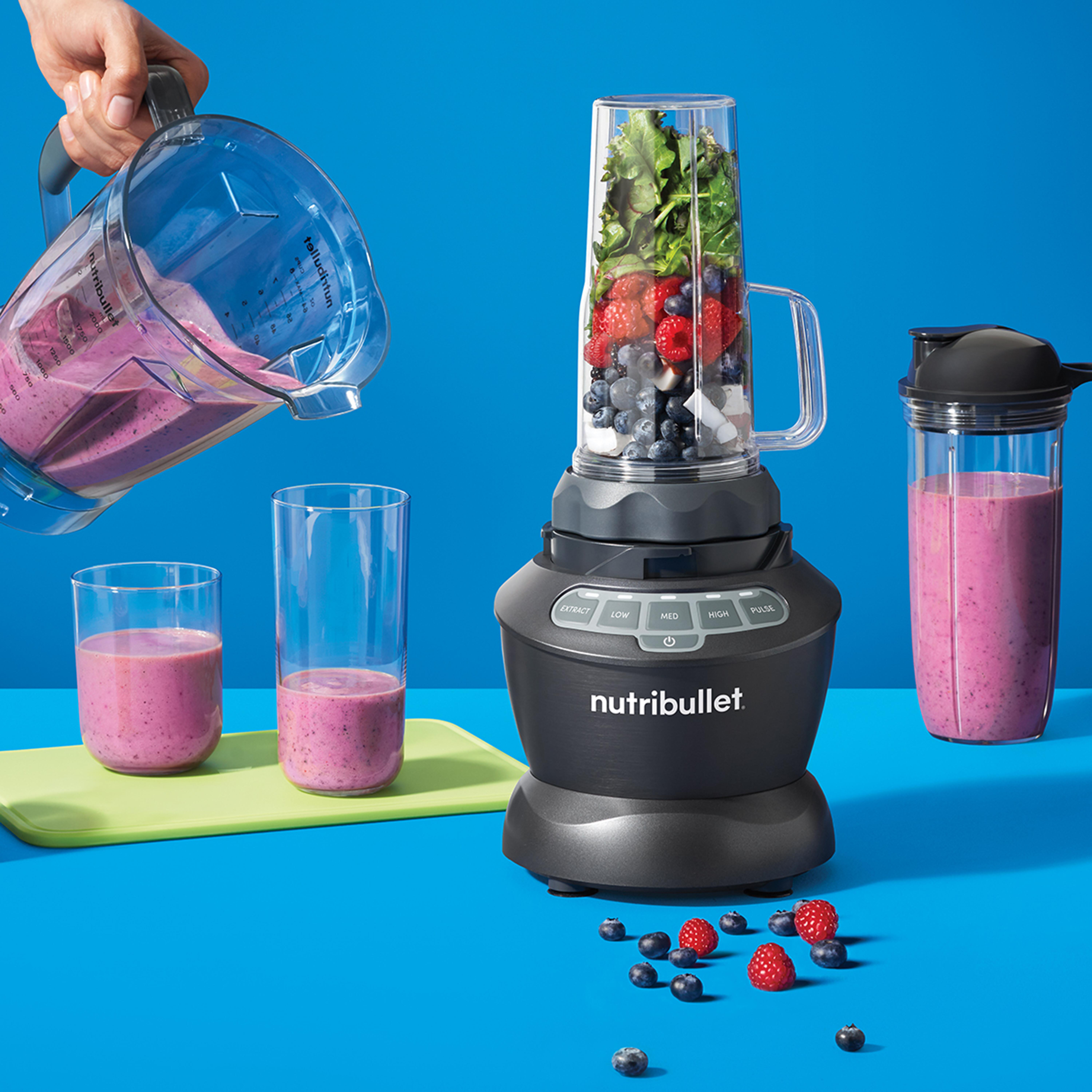 Ein Mixer mit Früchten und grünen Blättern. Ein Krug schüttet Smoothie in ein Glas.