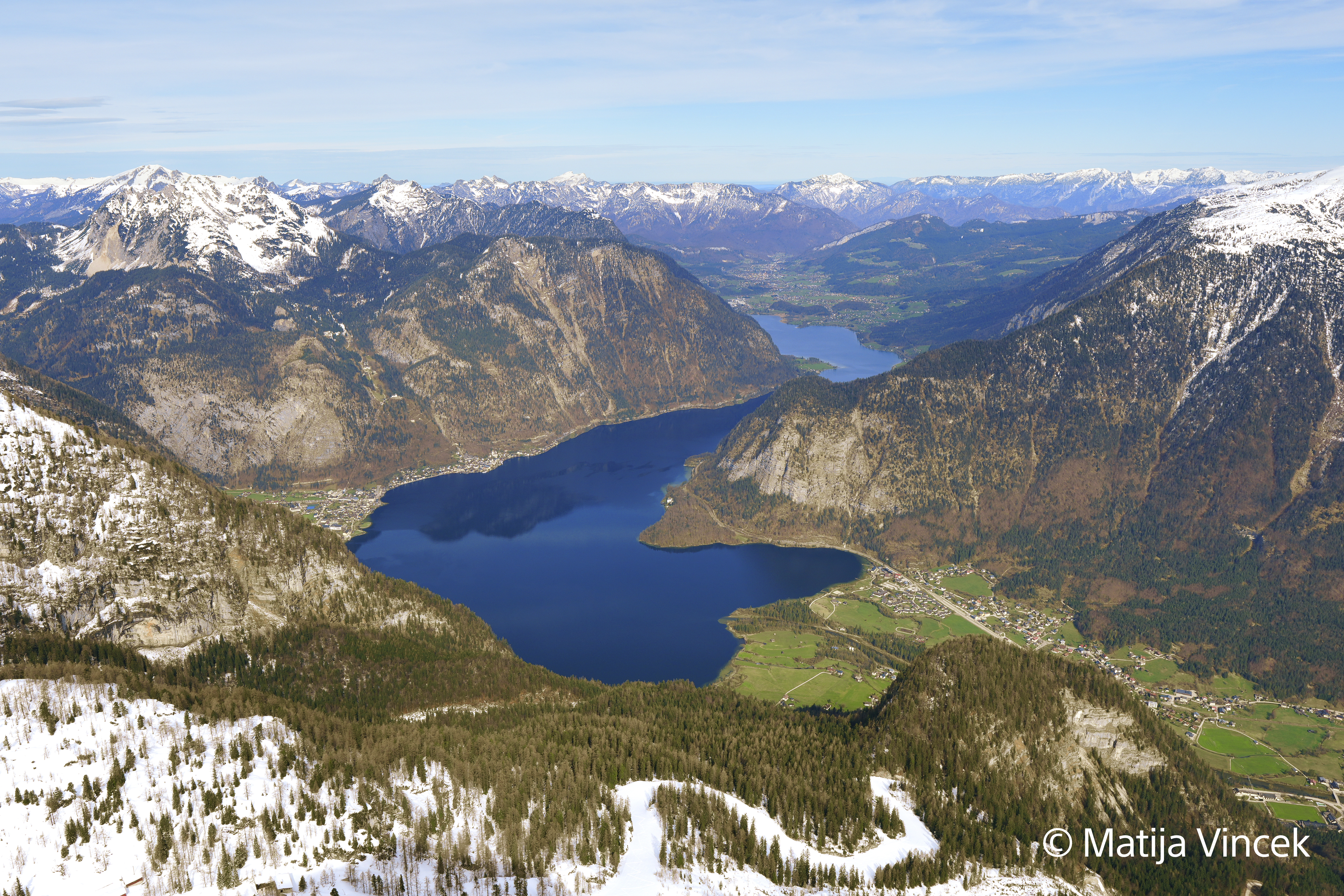 Luftaufnahme eines Sees, umgeben von schneebedeckten Bergen.