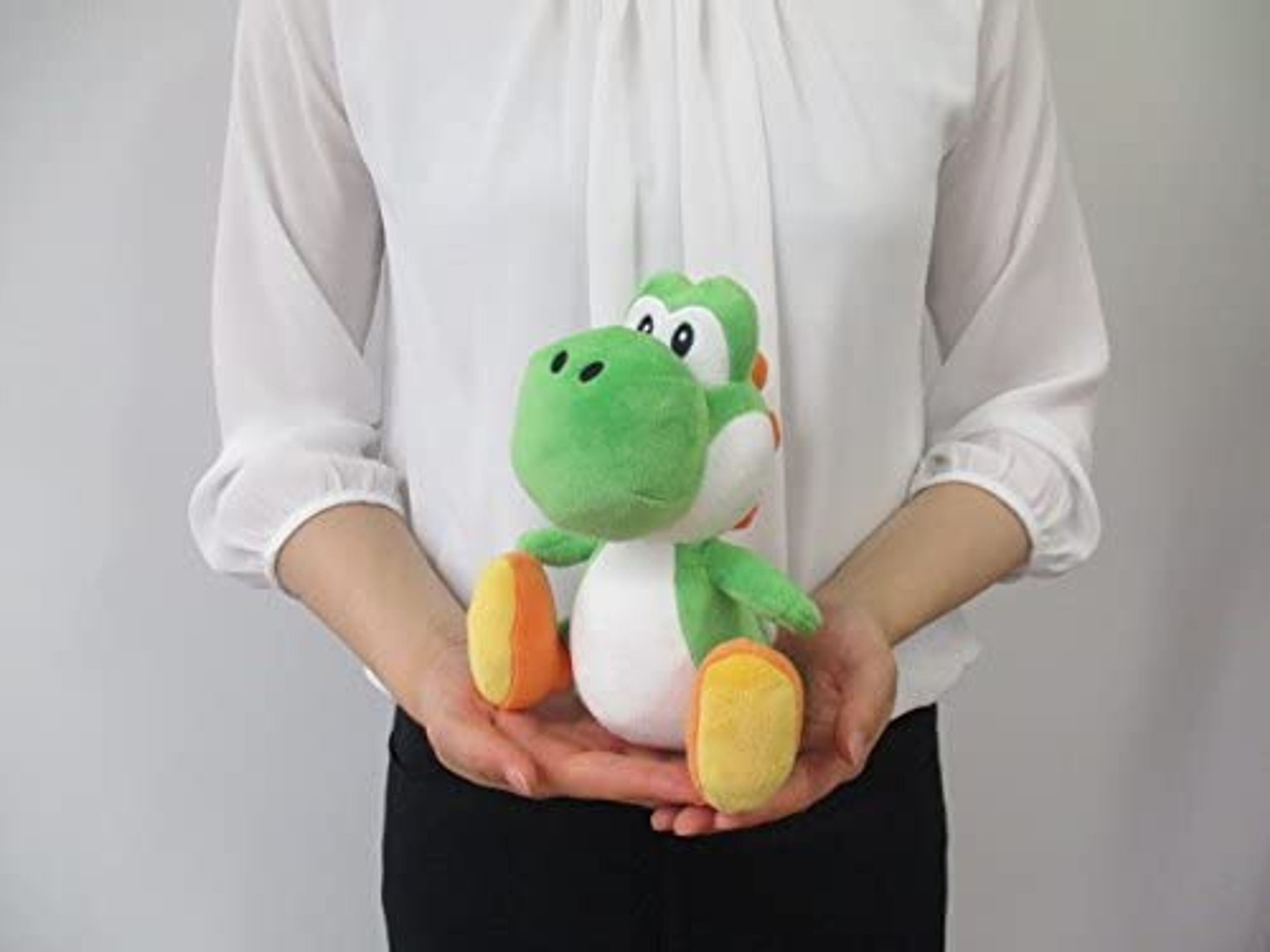 Eine Person hält ein grünes Yoshi-Plüschtier mit orangen und weißen Details.