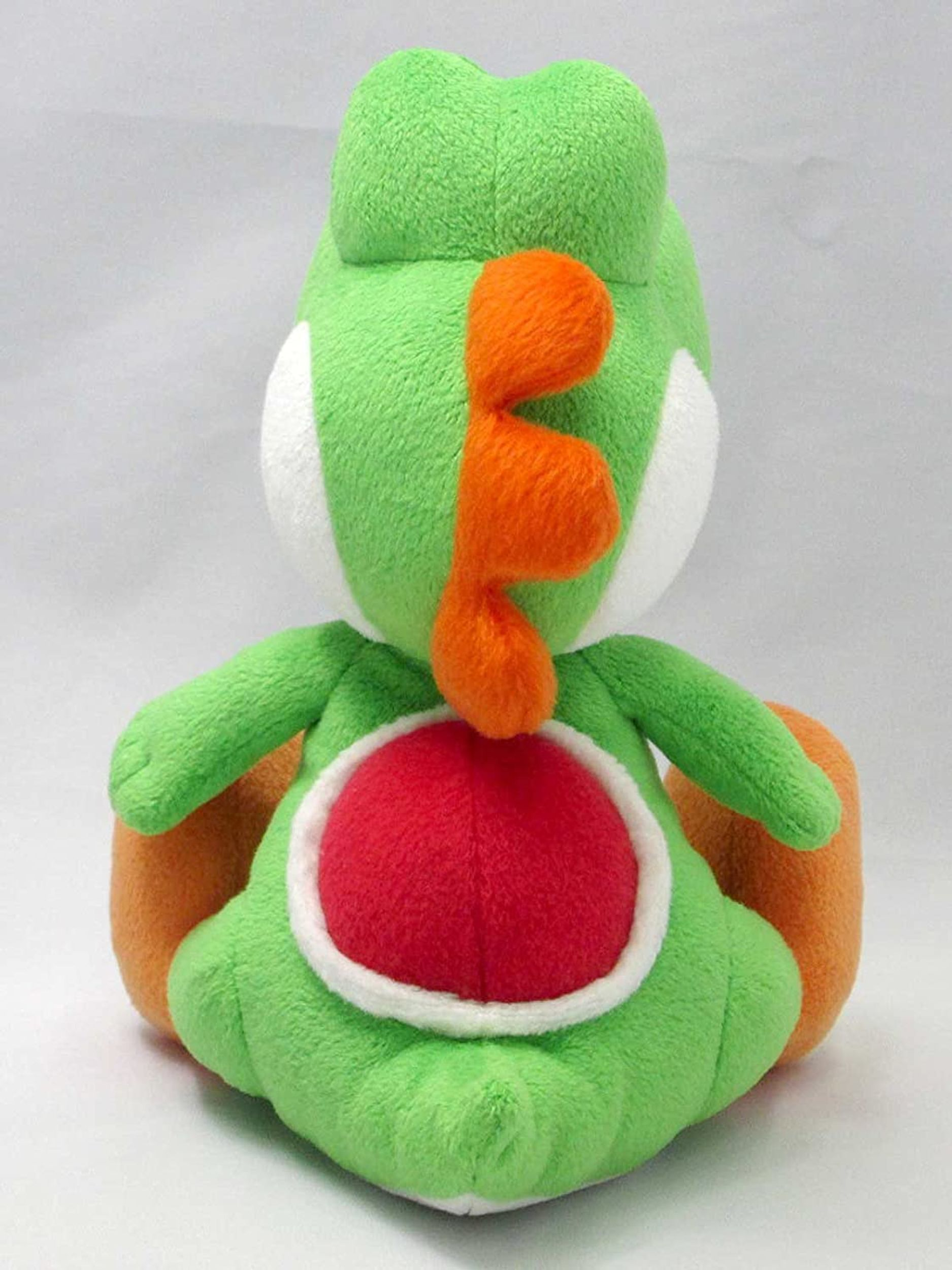 Ein grünes Yoshi-Plüschtier sitzt auf weißem Untergrund. Es hat weiße, orange und rote Details.