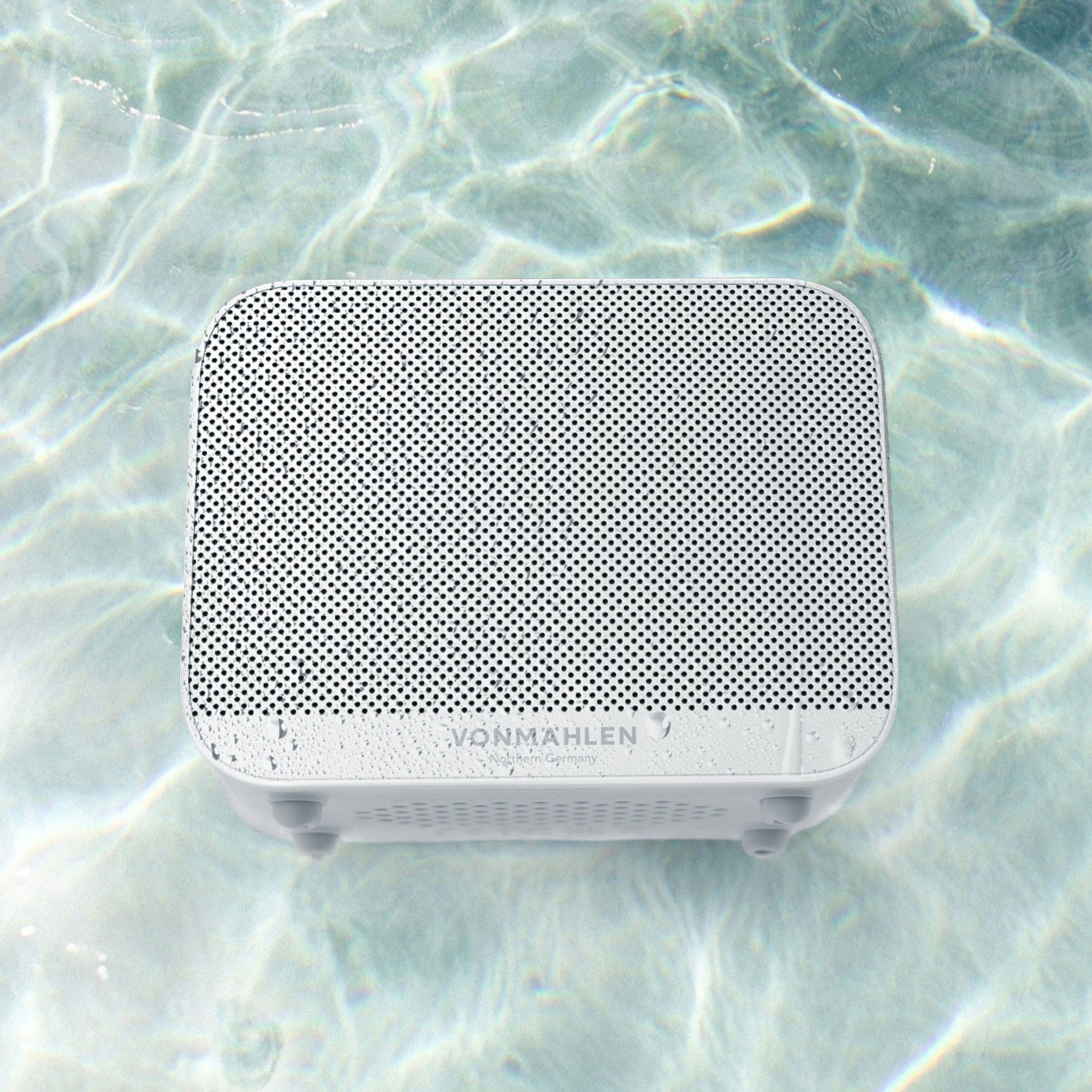 Ein weißer Lautsprecher schwimmt auf Wasser, mit einer weißen Netzfront und einem dunkel gefärbten Boden.