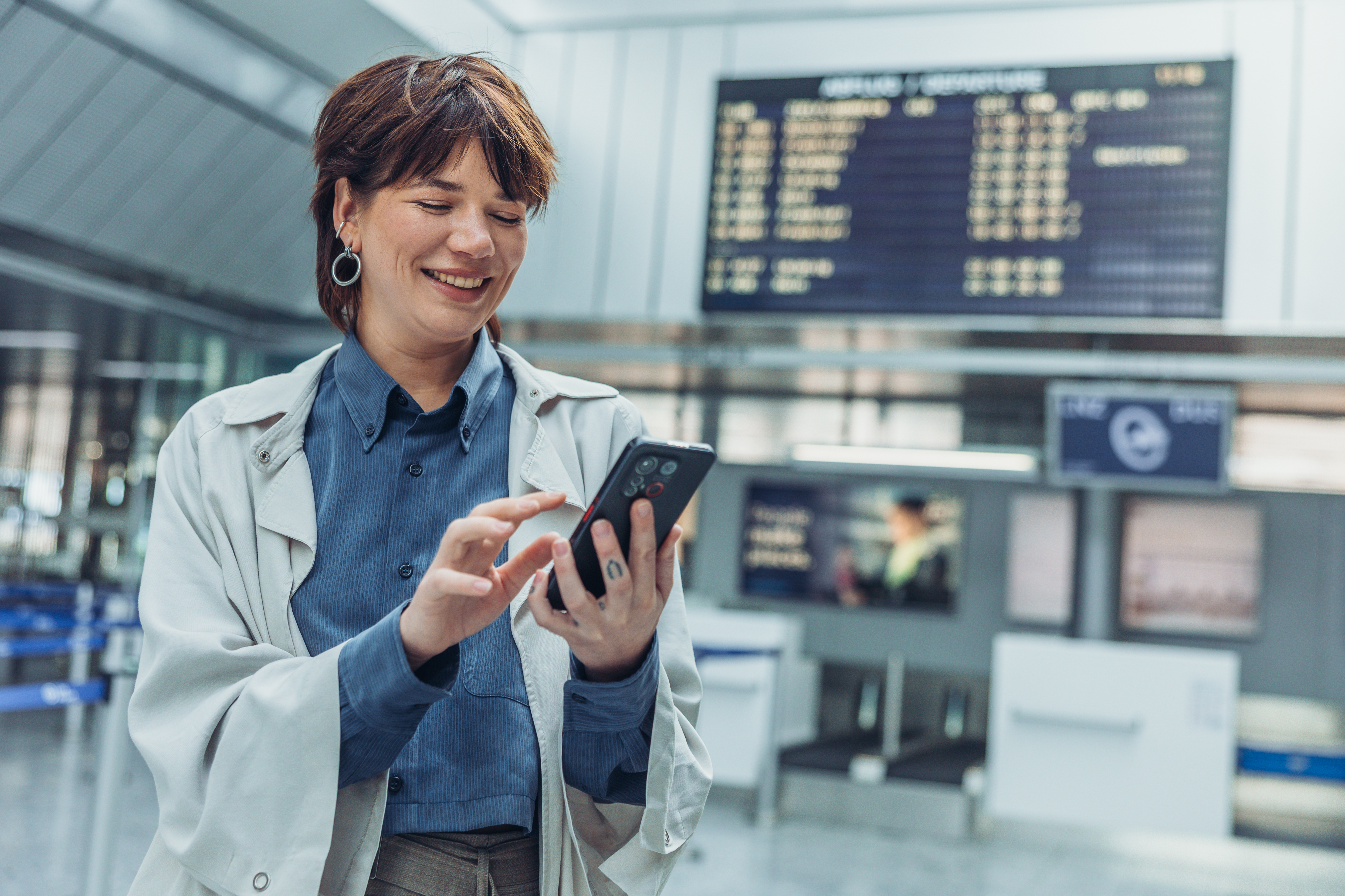 Frau im Trenchcoat benutzt Smartphone im Terminal.