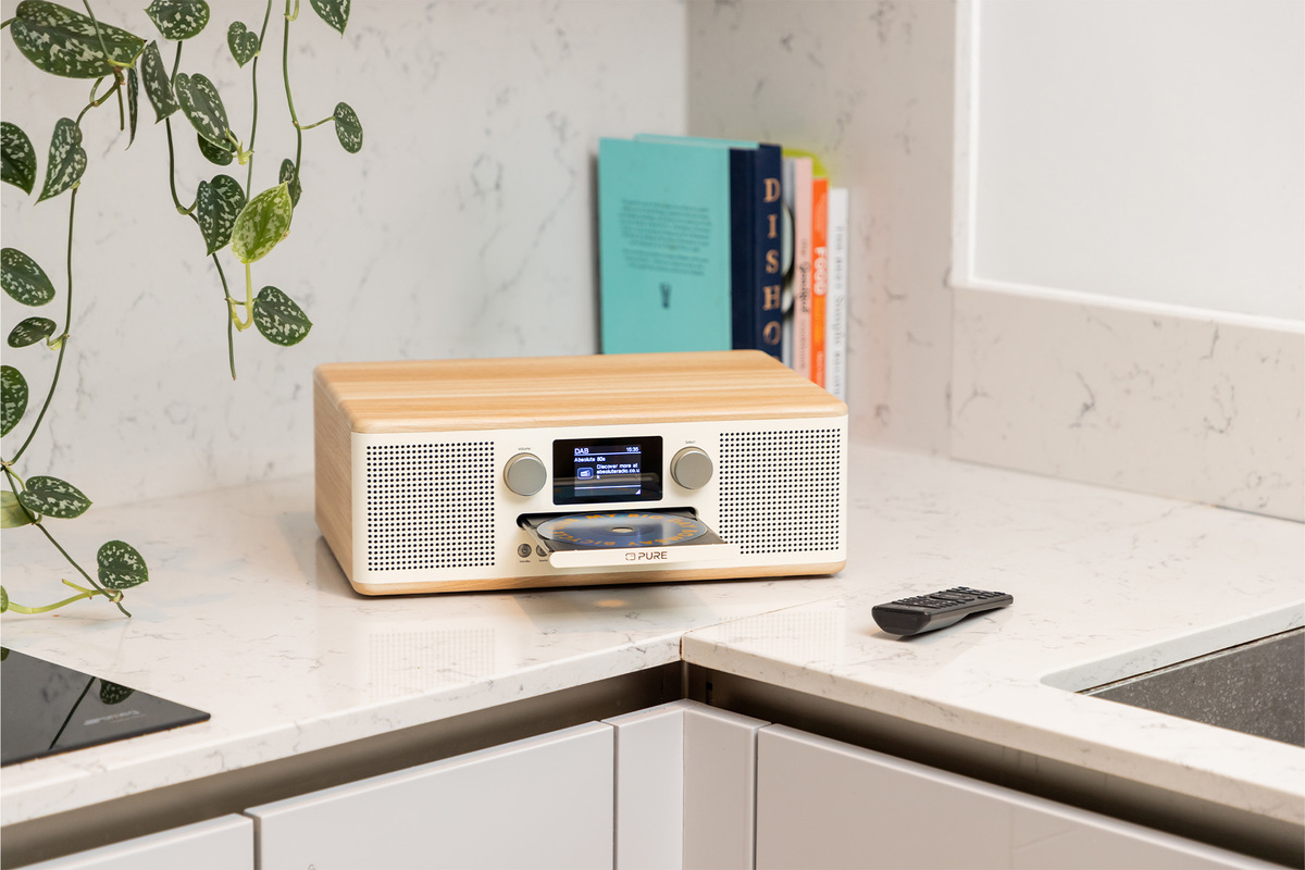 Une radio Pure avec un lecteur CD est sur un comptoir, avec des livres et une télécommande à proximité.