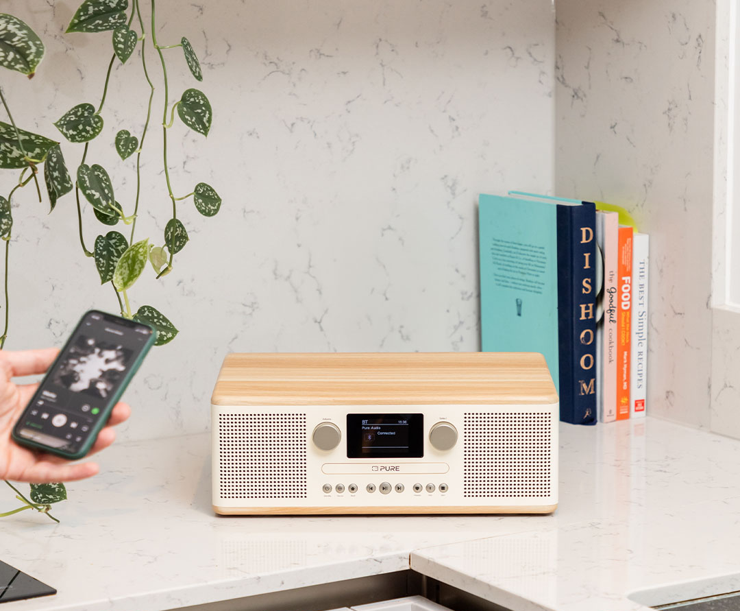 Une radio moderne est posée sur un comptoir. Une main tient un téléphone. Des livres sont placés à côté de la radio.
