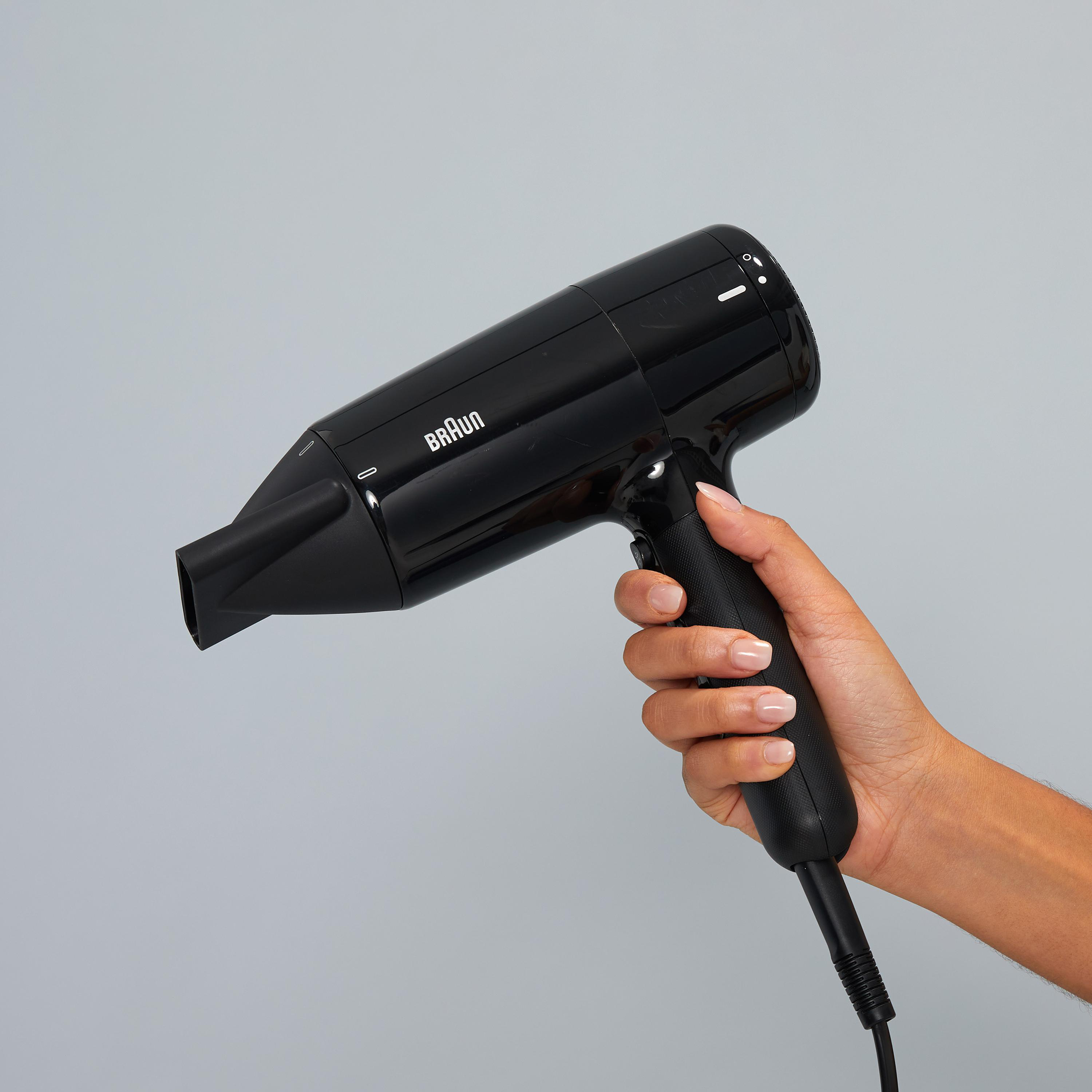 Hand hält einen schwarzen Braun Haartrockner vor grauem Hintergrund.