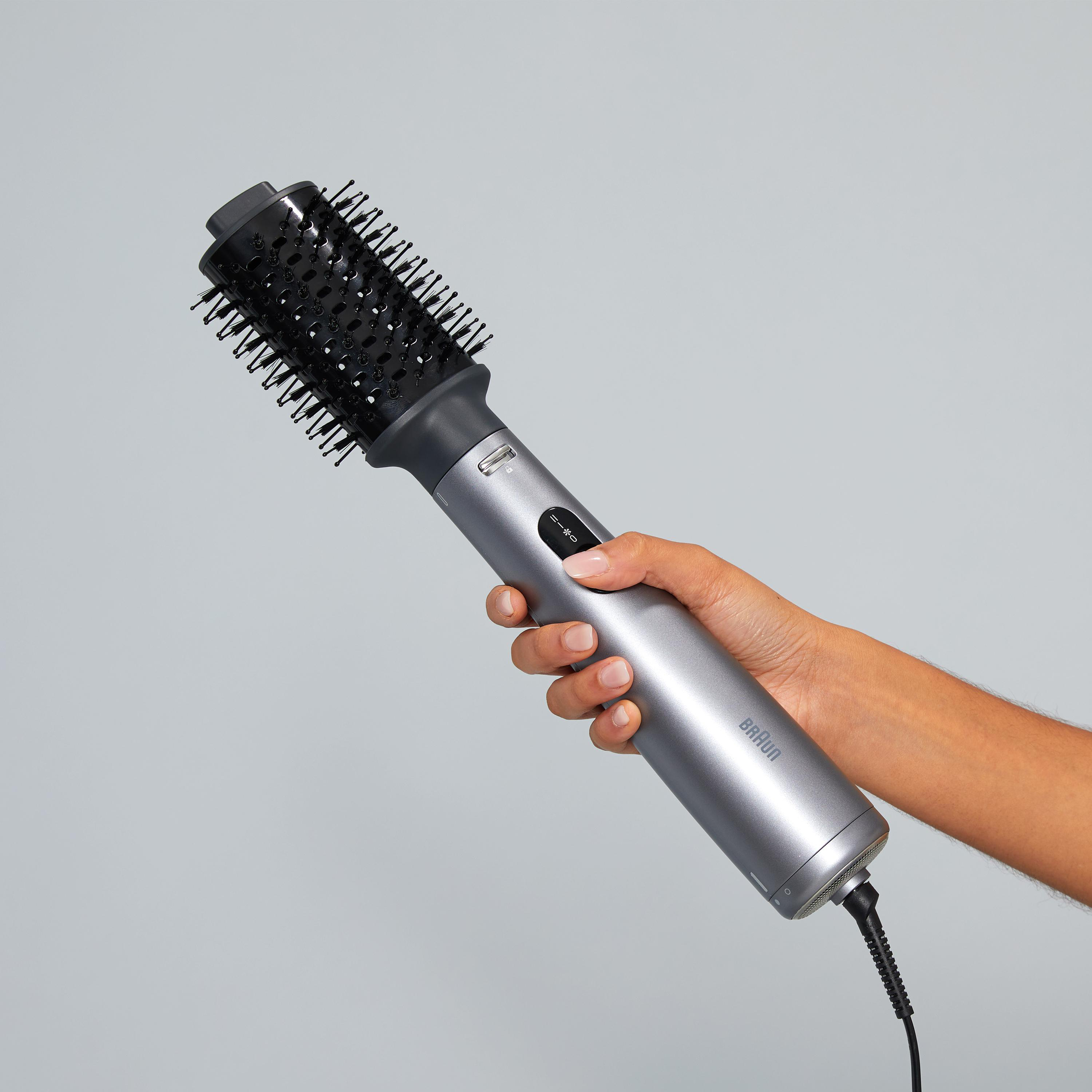 Die Hand einer Frau, die eine graue Braun Haarbürste hält, vor hellgrauem Hintergrund.
