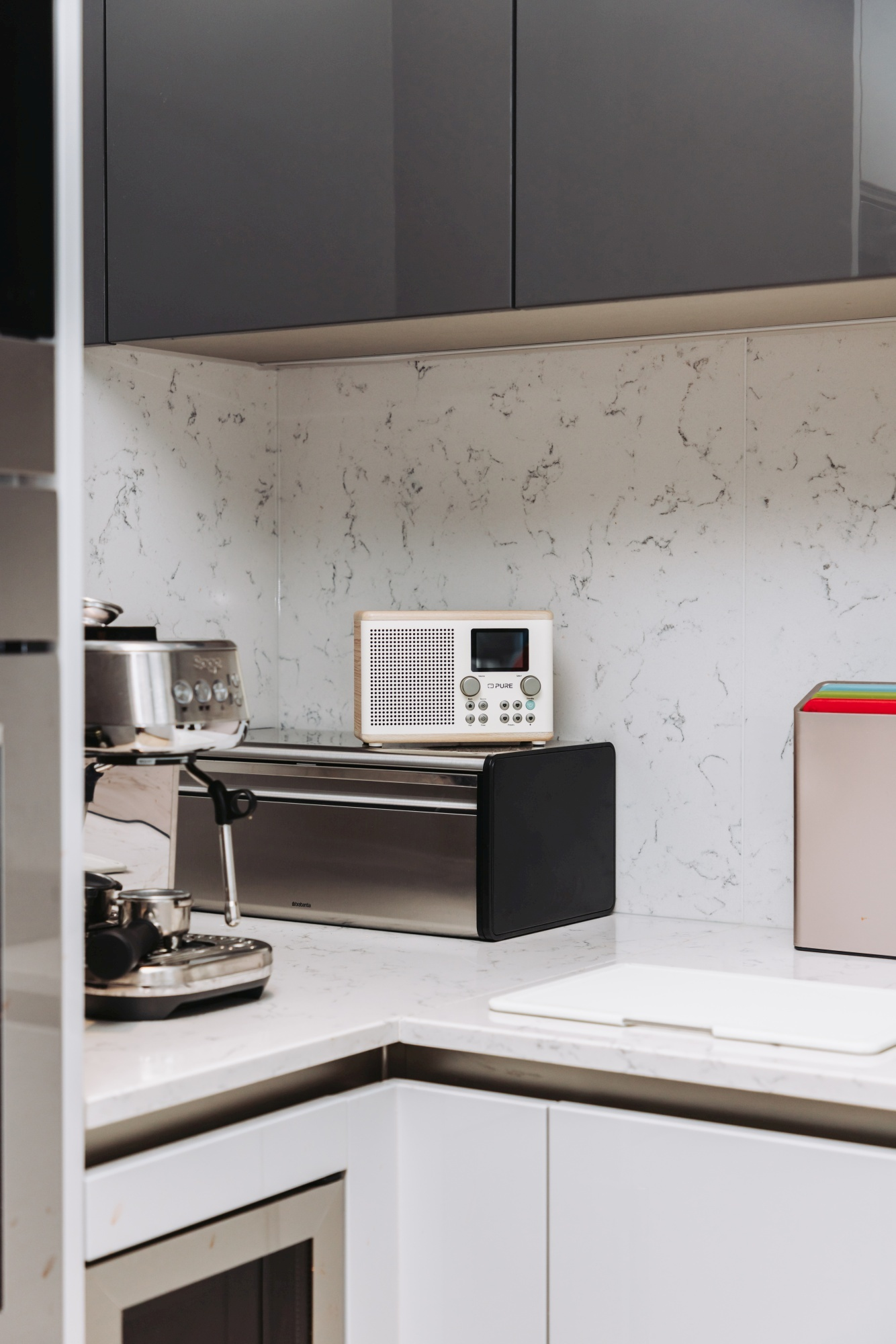 Eine Küchenszene mit einer Kaffeemaschine, einem Toaster und einem Radio. Die Geräte stehen auf einer Arbeitsplatte mit Marmoreffekt.