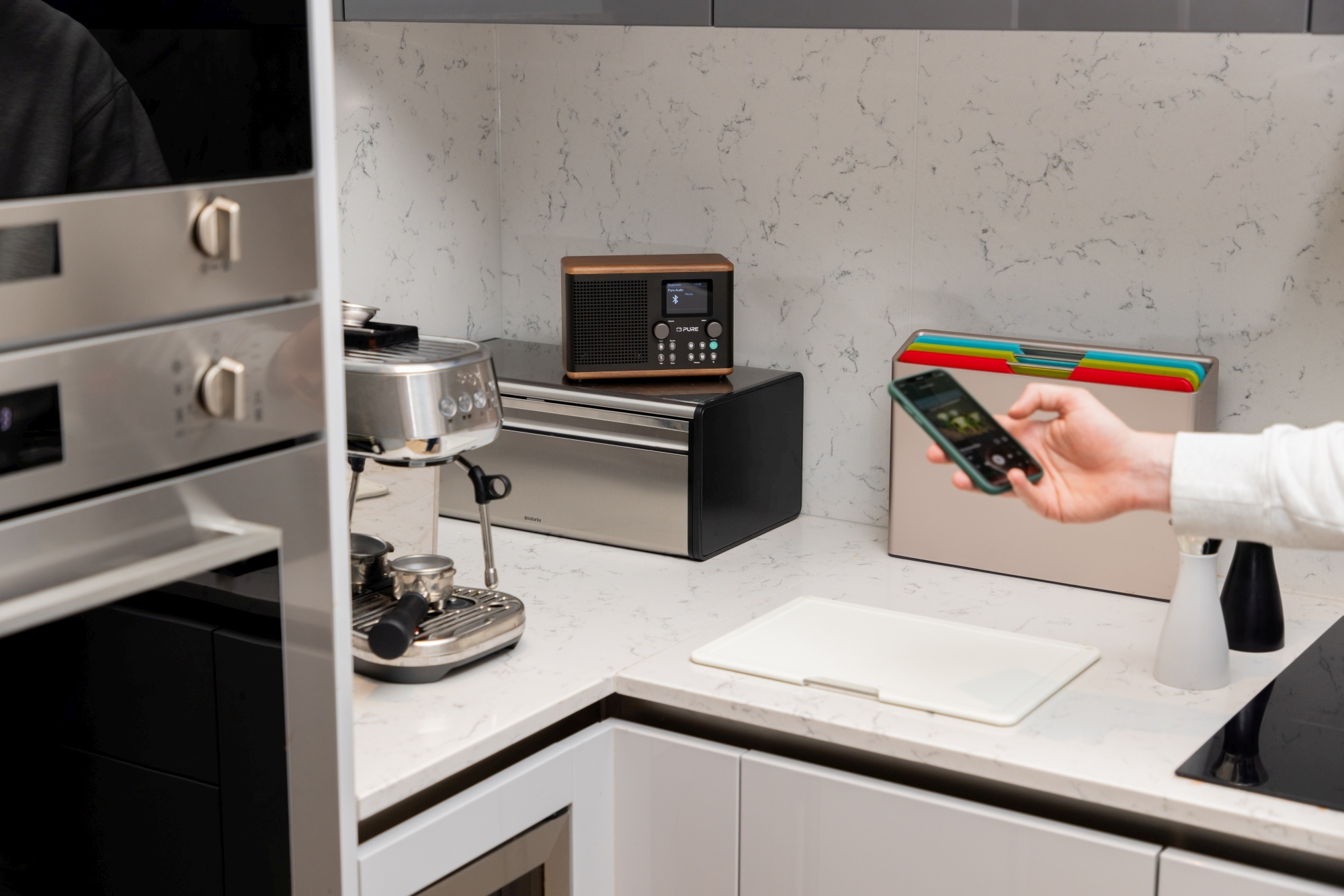 Un comptoir de cuisine avec des appareils : cafetière, radio et planche à découper.