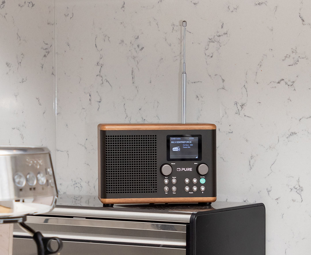 Une radio en bois avec un panneau avant noir, un écran et des boutons, sur une surface argentée.