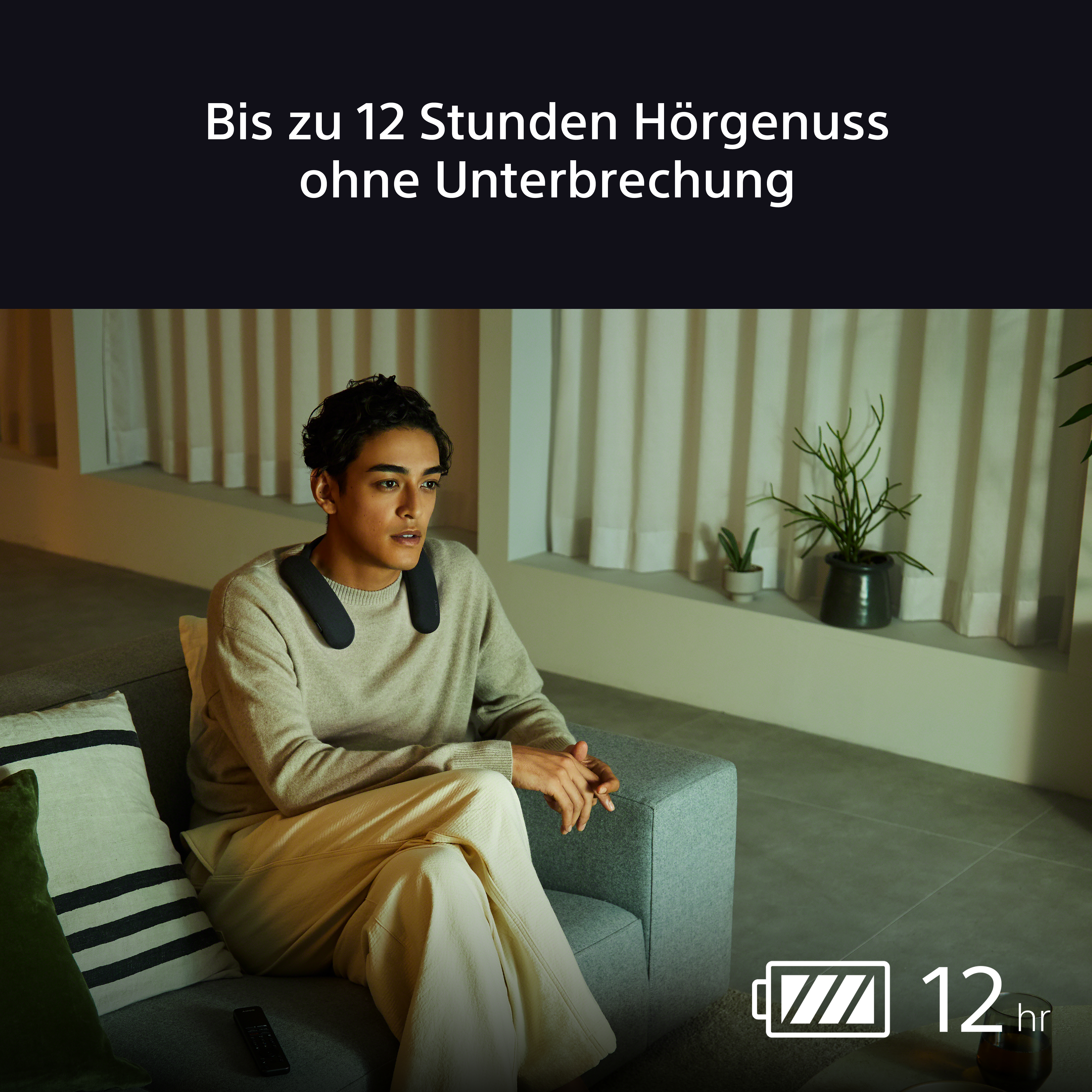 Mann mit Nackenlautsprecher auf dem Sofa, sieht fern. Text: Bis zu 12 Stunden ununterbrochenes Hören.