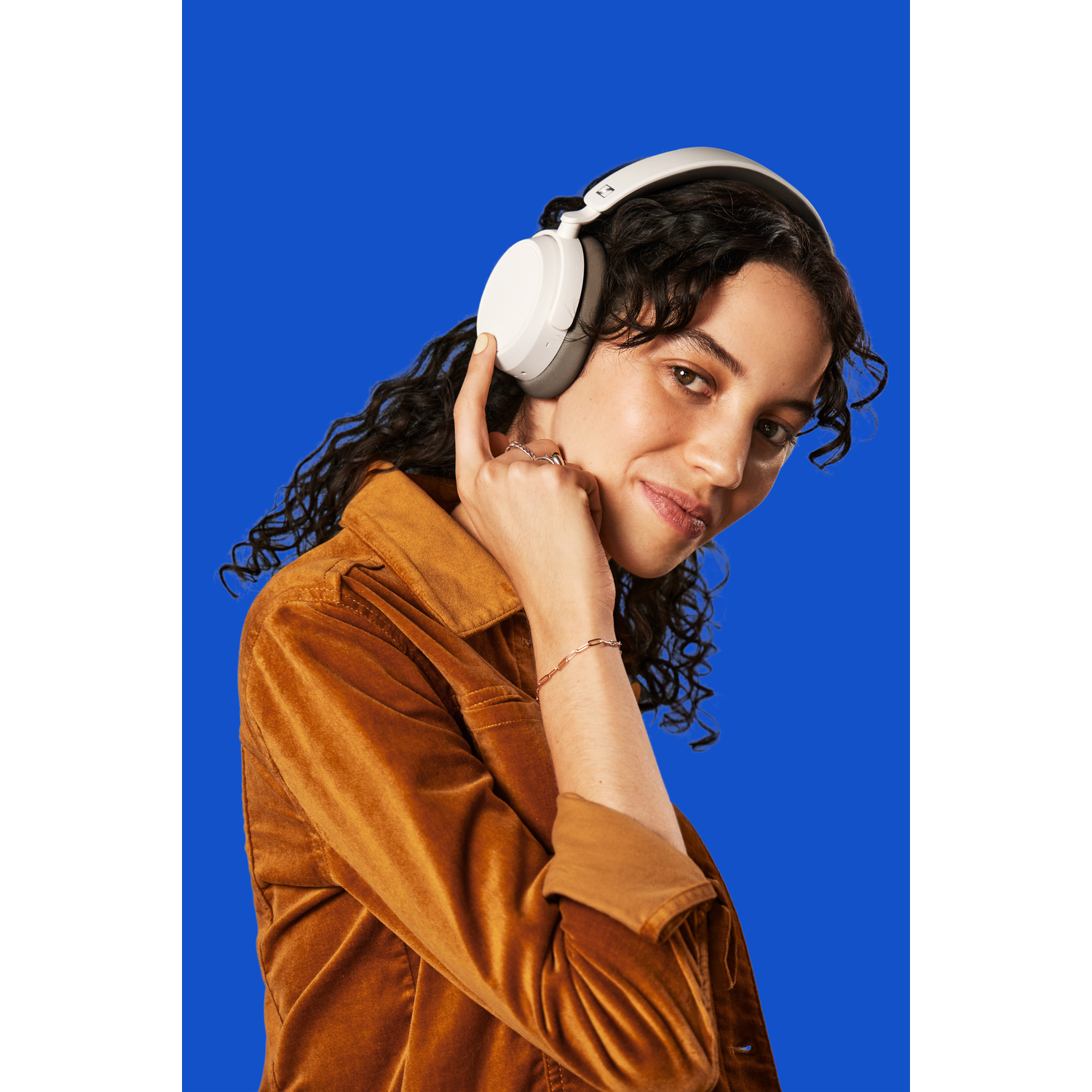 A woman with white headphones smiles at the camera against a blue background.