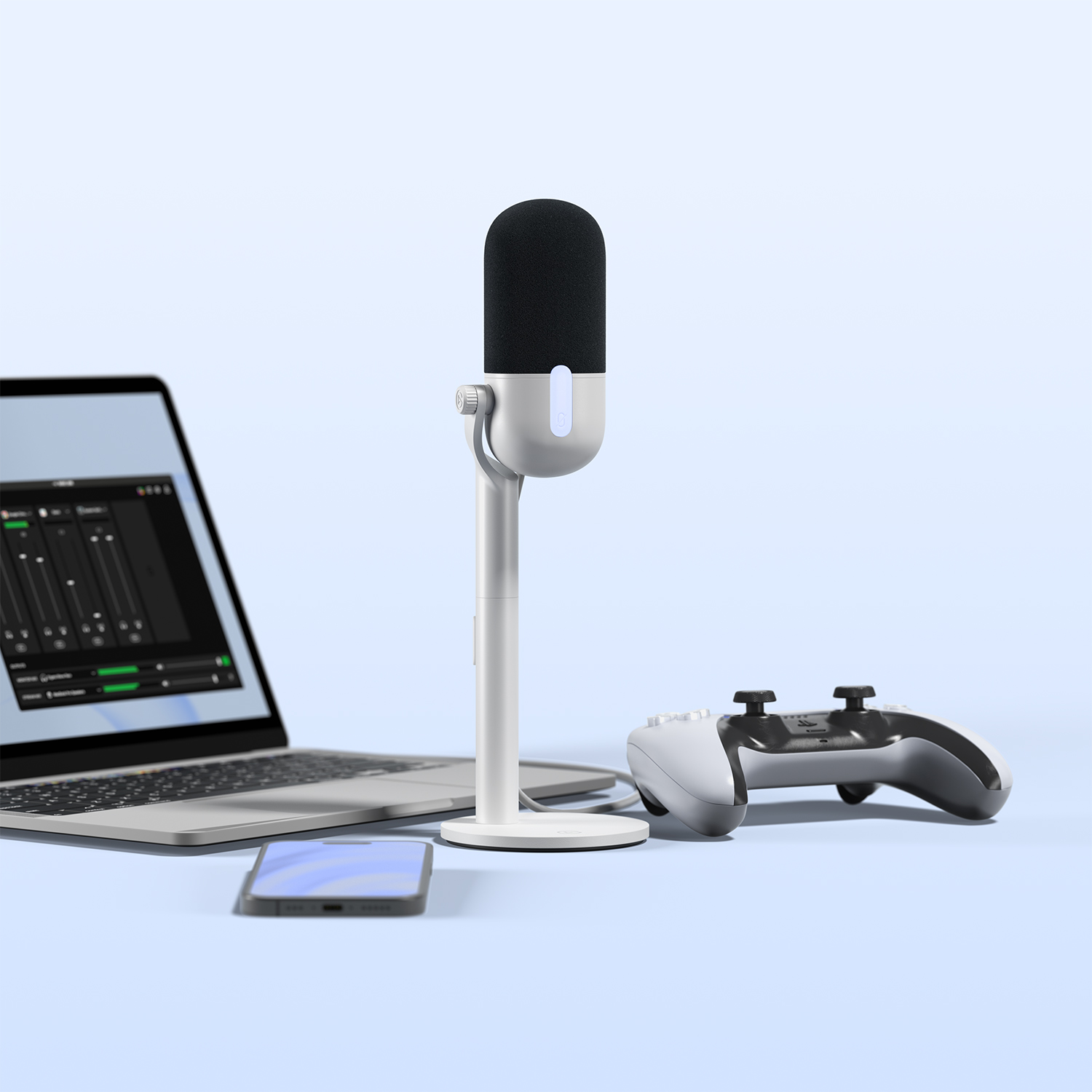 Un microfono su un supporto, un laptop, uno smartphone e un controller di gioco su una superficie azzurra.