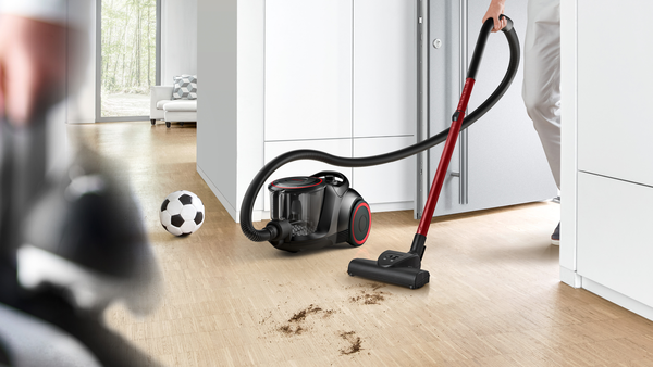 Bir kişi, zeminde bir futbol topu bulunan bir odayı bir elektrik süpürgesiyle süpürüyor.