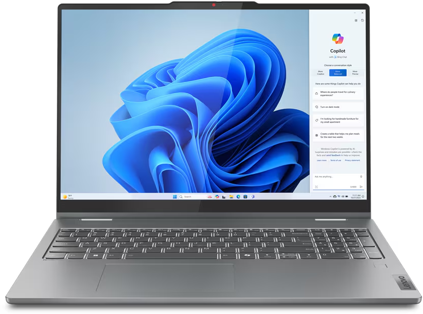 Silberner Lenovo-Laptop geöffnet, zeigt Windows Copilot-Oberfläche mit blauem Hintergrund. Der Laptop steht auf einem Tisch.