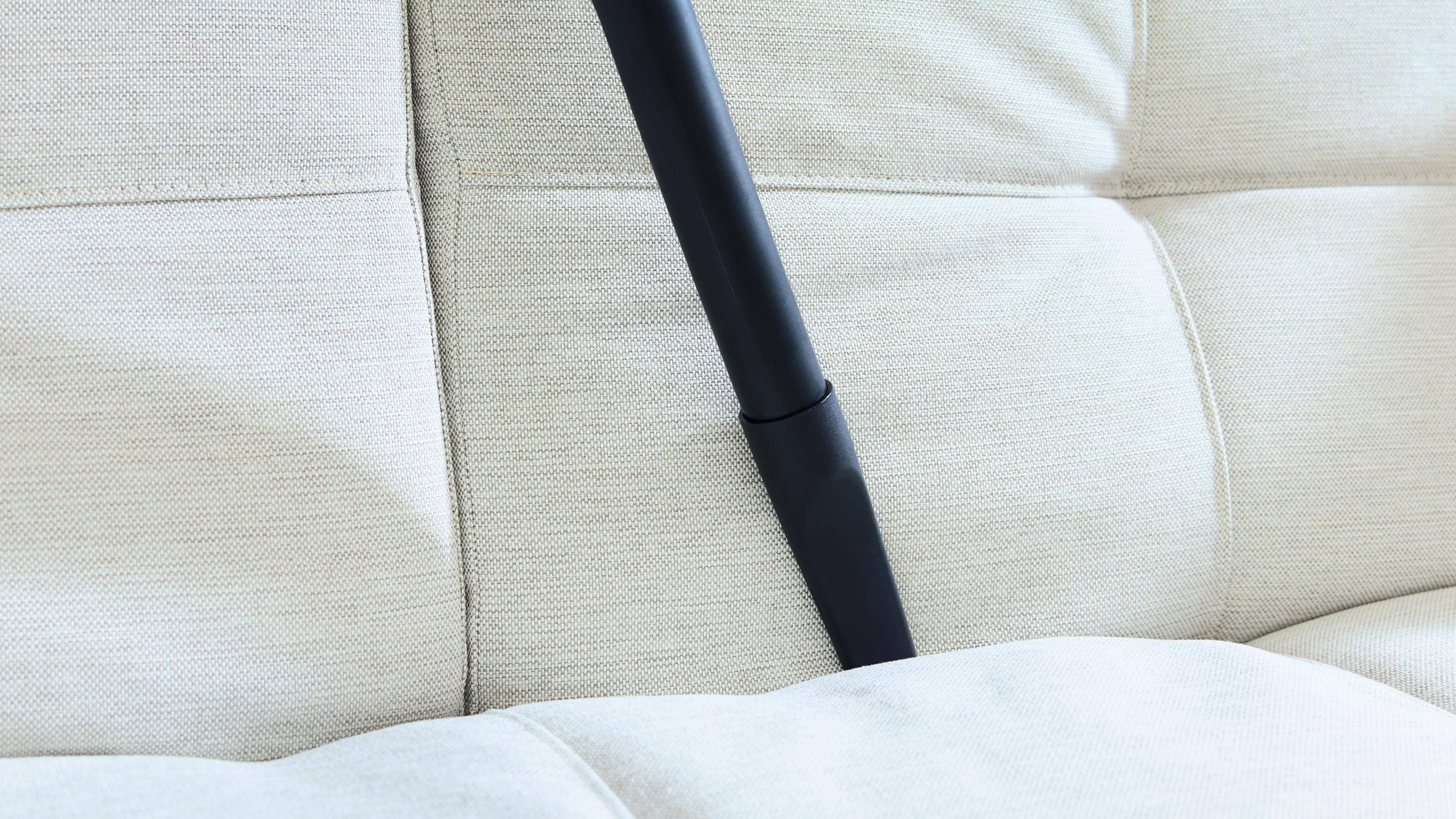 Schwarze Staubsaugerdüse reinigt ein weißes Sofa.
