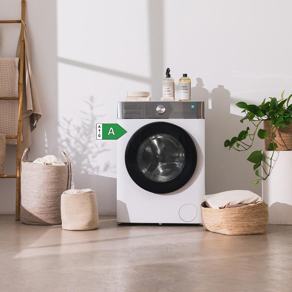 Una lavadora blanca con puerta negra, junto a cestos y plantas.