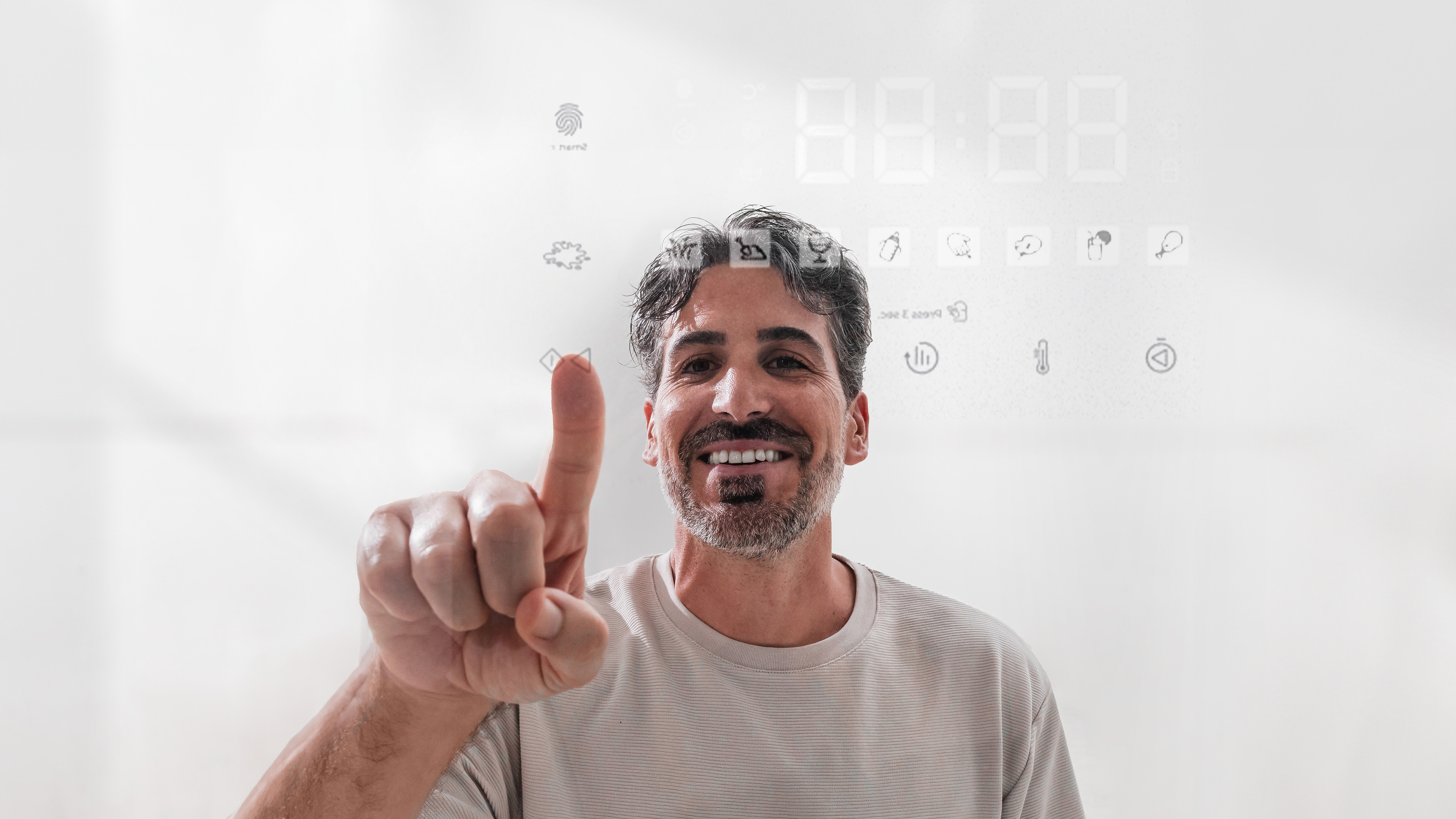 Hombre señalando una pantalla transparente, con iconos digitales y números encima. Sonríe, fondo claro.