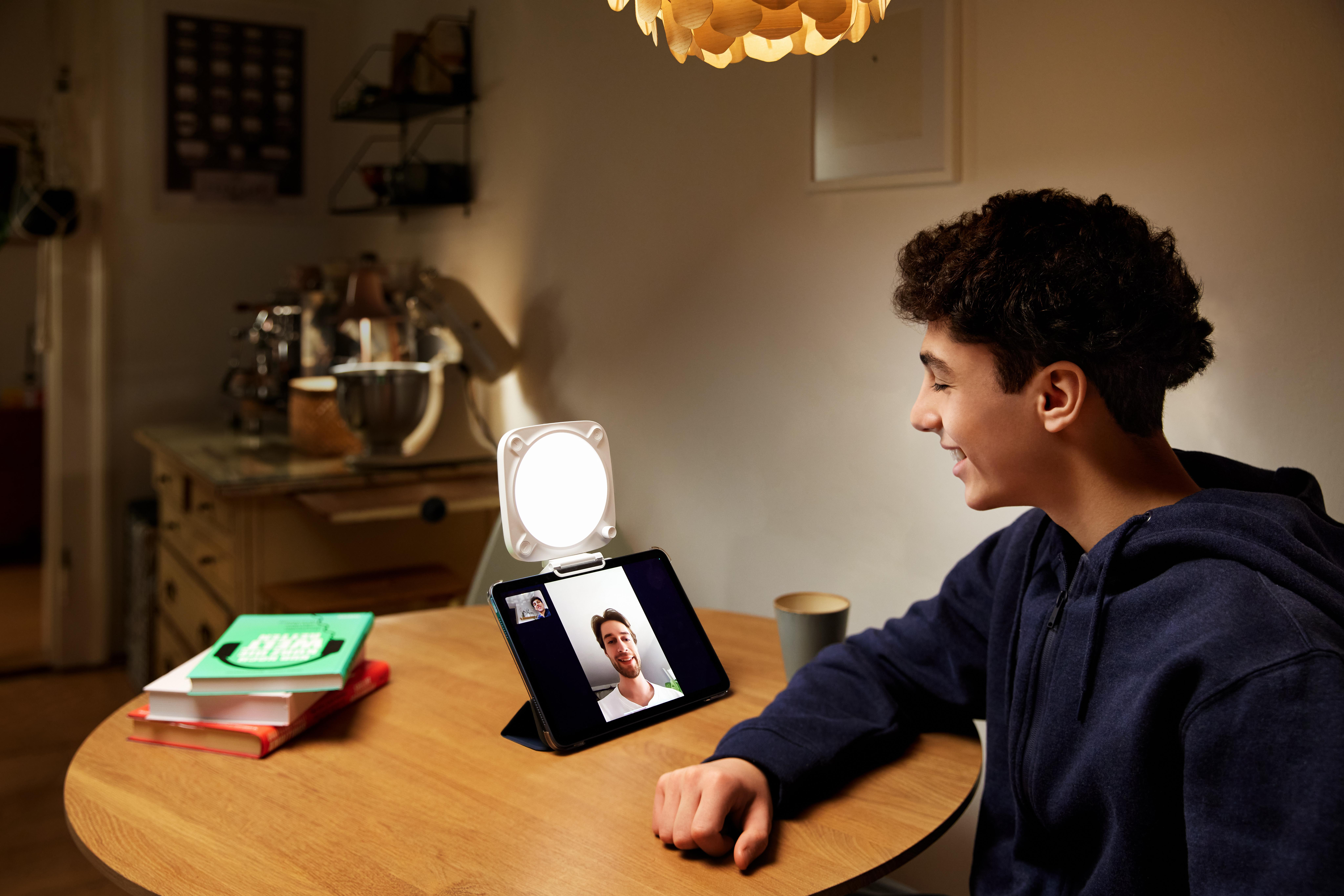Teenager beim Videoanruf. Tablet auf Tisch mit Lampe, die Anruf und Tisch beleuchtet.