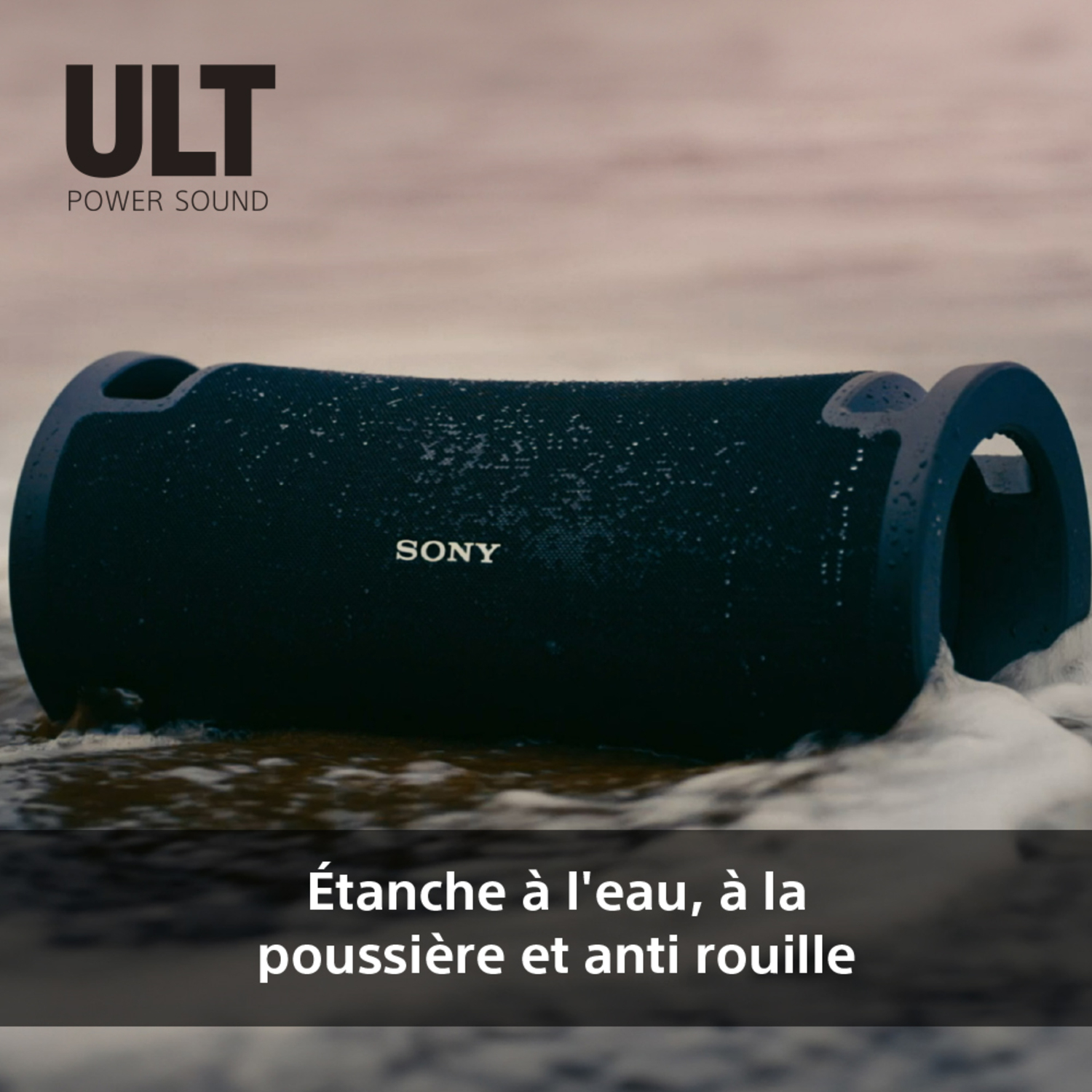 Un haut-parleur bleu et noir sur une plage. Il est cylindrique et porte le mot SONY.